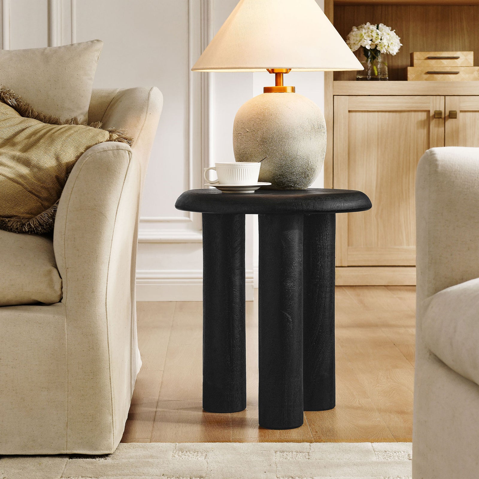 Black mango wood side table with bold round top and three pillar legs styled in a warm living room || EEI-7284-BLK || front_angle_room