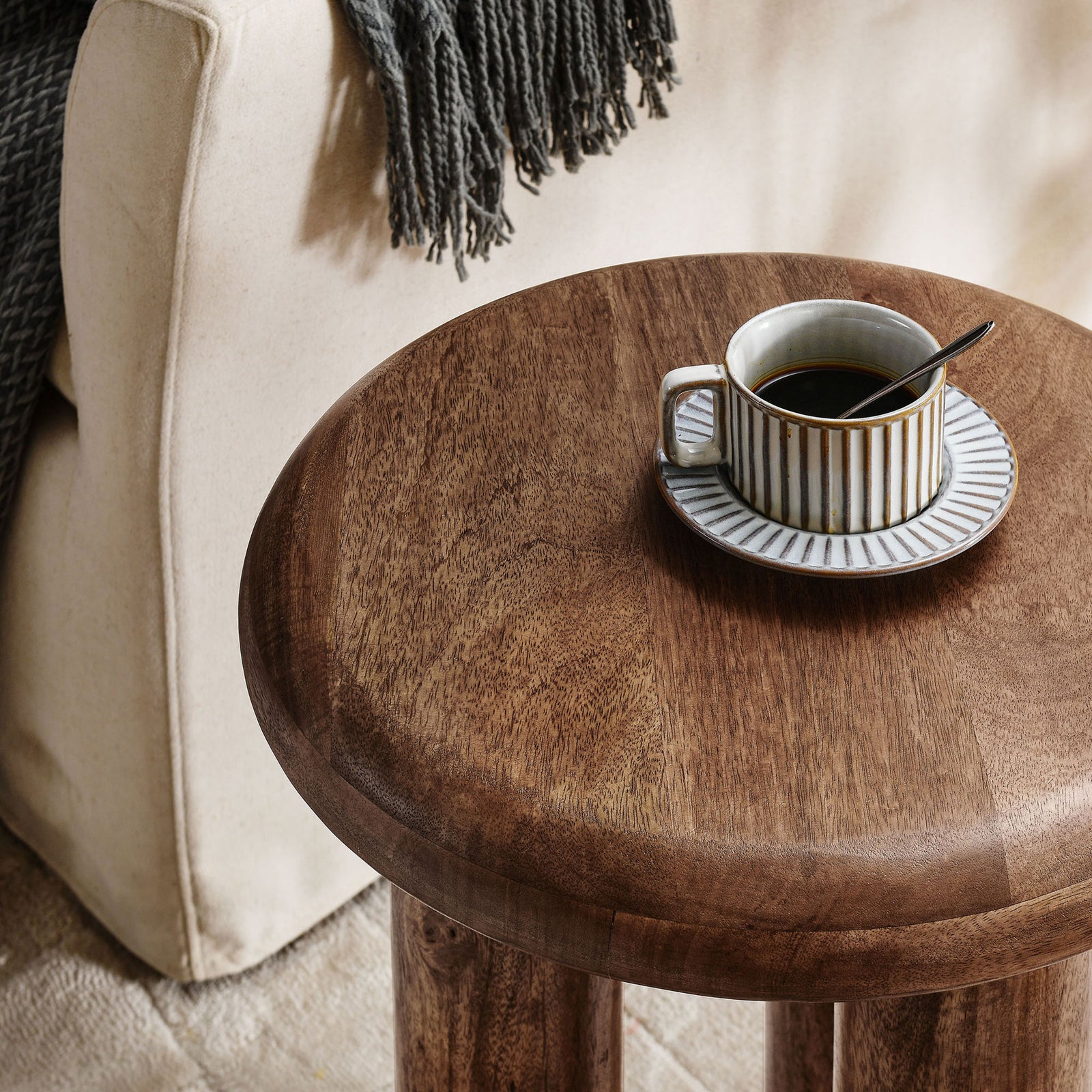 Mavina side table styled with a coffee cup beside a cozy sofa, showing its warm walnut tabletop. || EEI-7284-WAL || detail_room