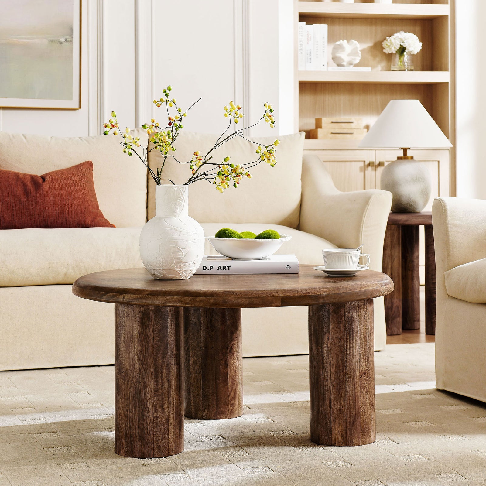 Solid mango wood coffee table anchors the room with its rounded silhouette and three-leg design. || EEI-7286-WAL || front_angle_room