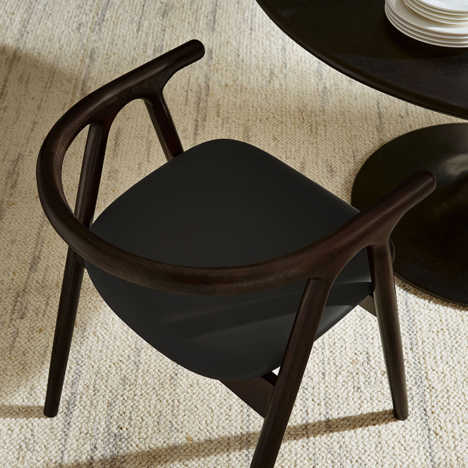Henry dining chair pulled up to a round table, featuring a black vegan leather seat and dark wood frame || EEI-7291-BLK || top_angle_room