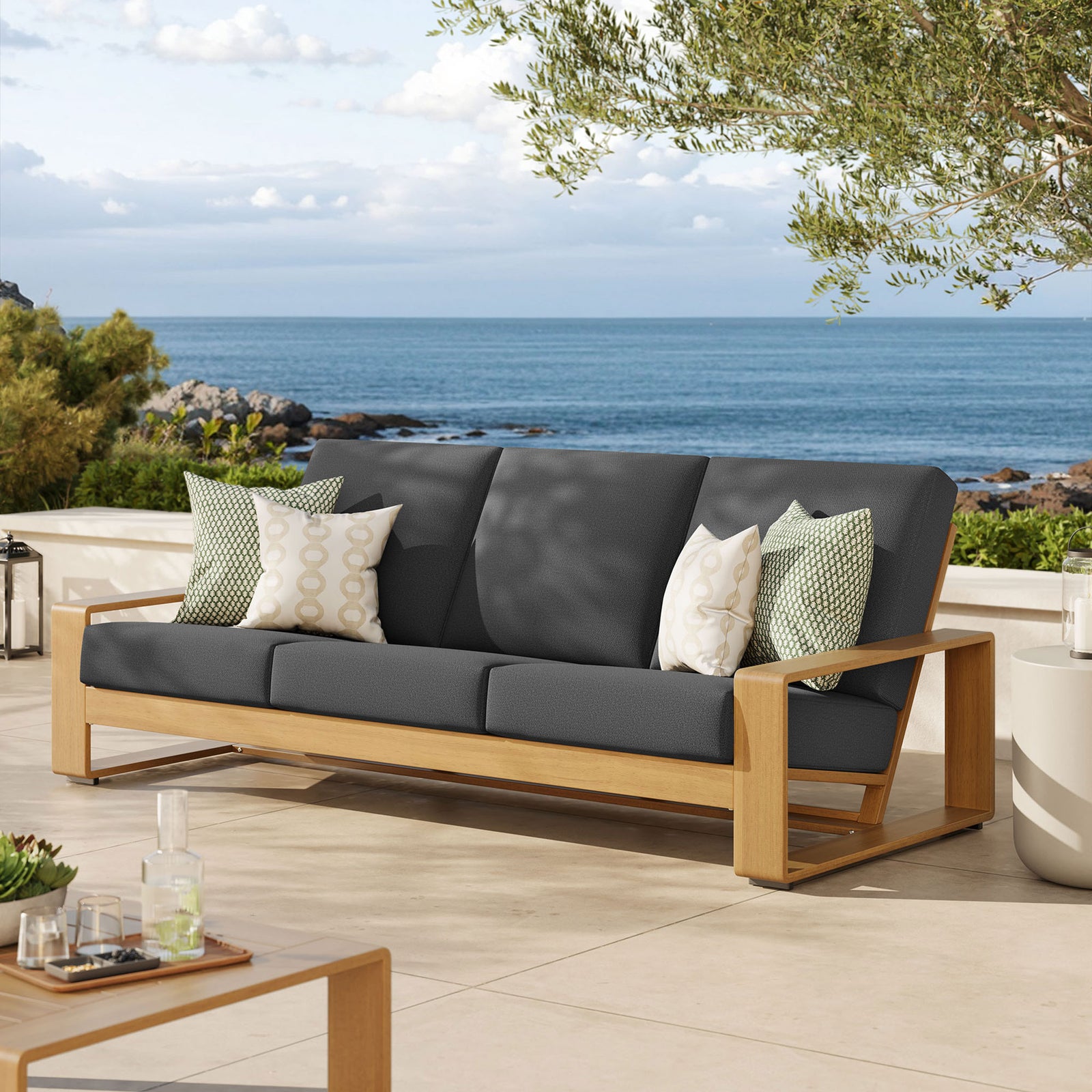 Charcoal cushioned outdoor sofa with natural faux wood frame anchoring a relaxed coastal patio seating area || EEI-7298-CHA-NAT || front_angle_room
