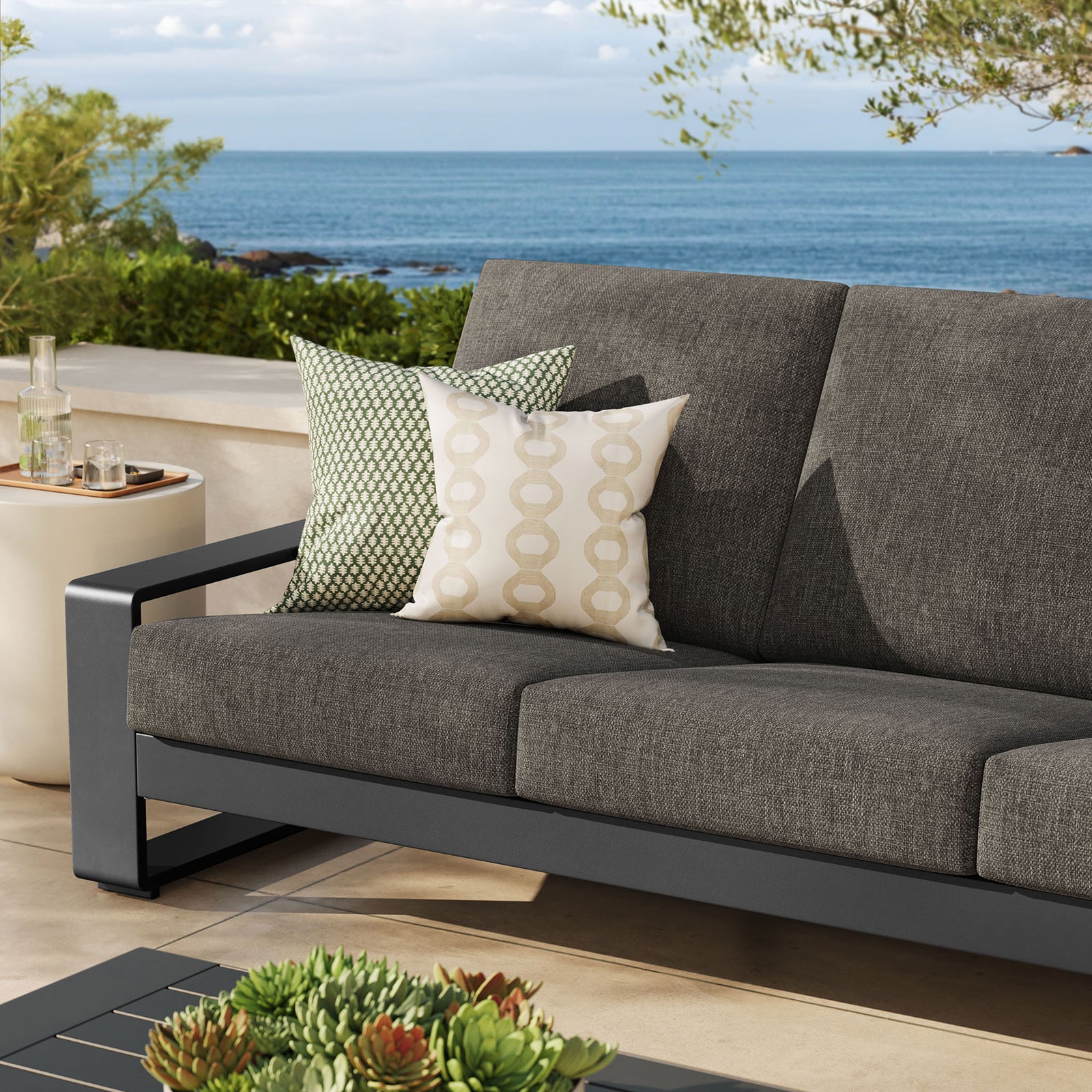 Smoke gray outdoor sofa styled with patterned throw pillows beside the sea, adding depth to the neutral patio || EEI-7302-SMO-GRY || detail_room