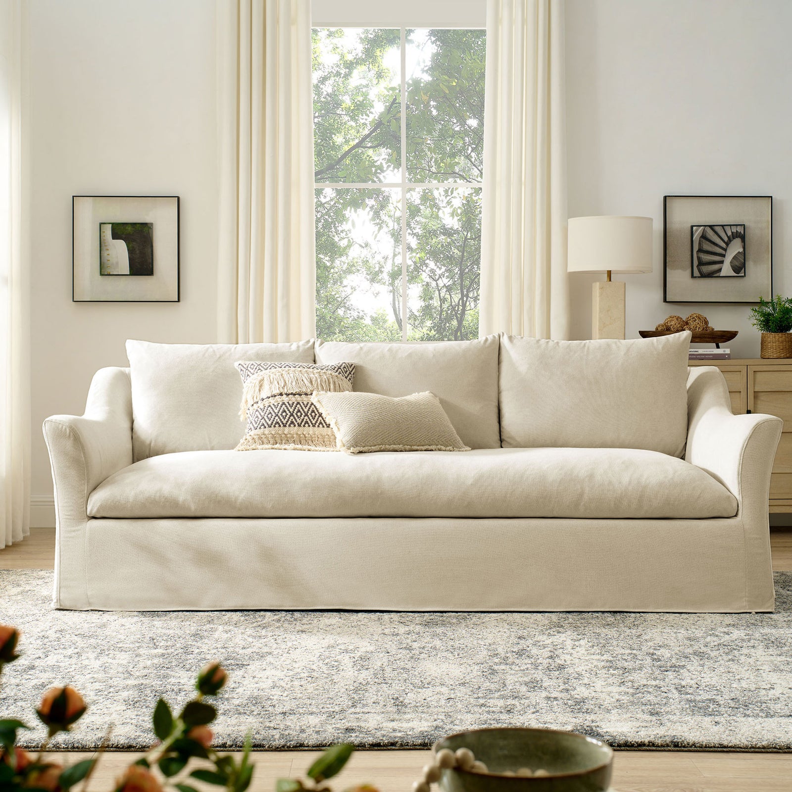 Light linen blend sofa centered in an airy living room with large window, framed art, and textured area rug || EEI-7310-LIN || front_room