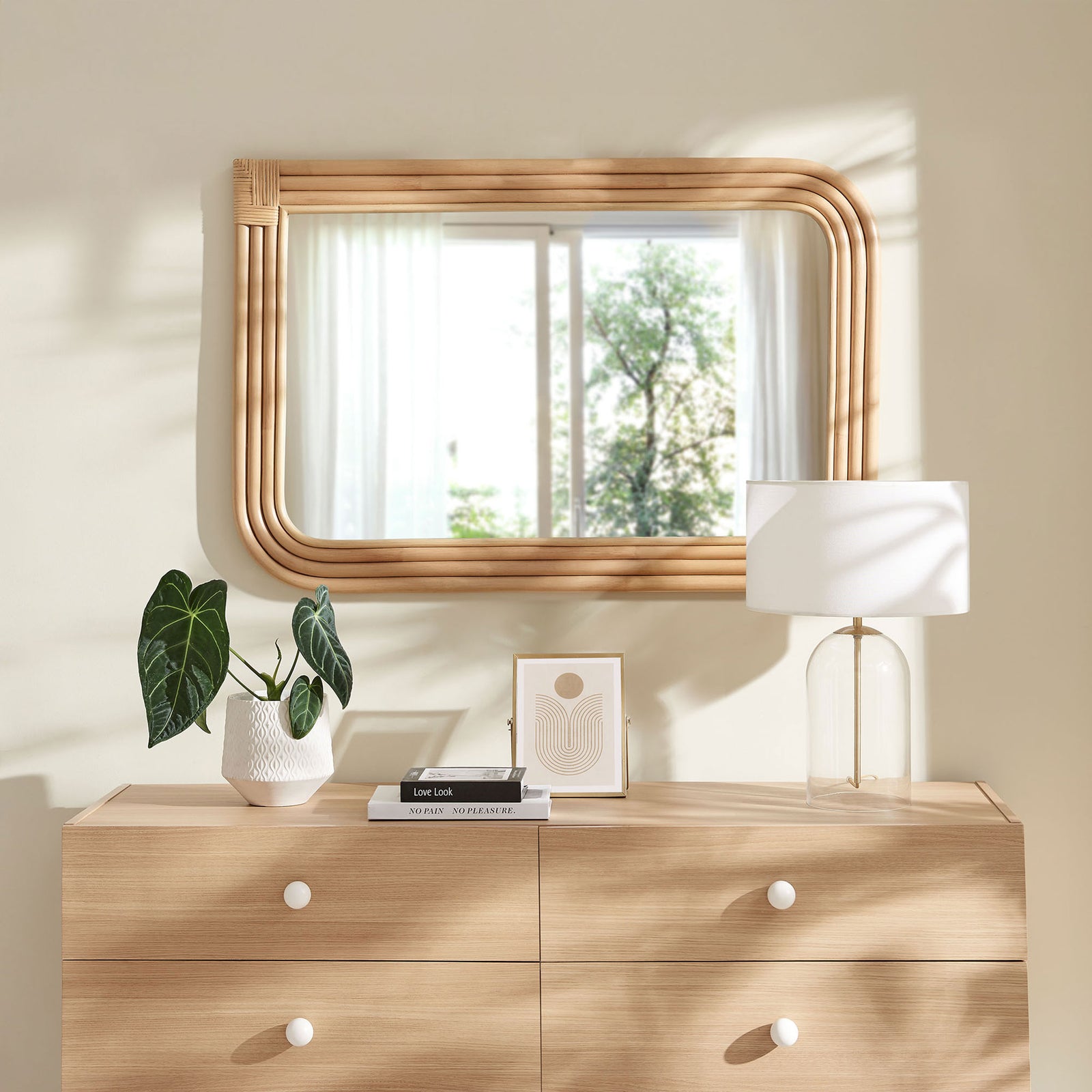 Corsica curved rectangle rattan mirror styled above a dresser in a bright, relaxed bedroom || EEI-7368-NAT || front_room