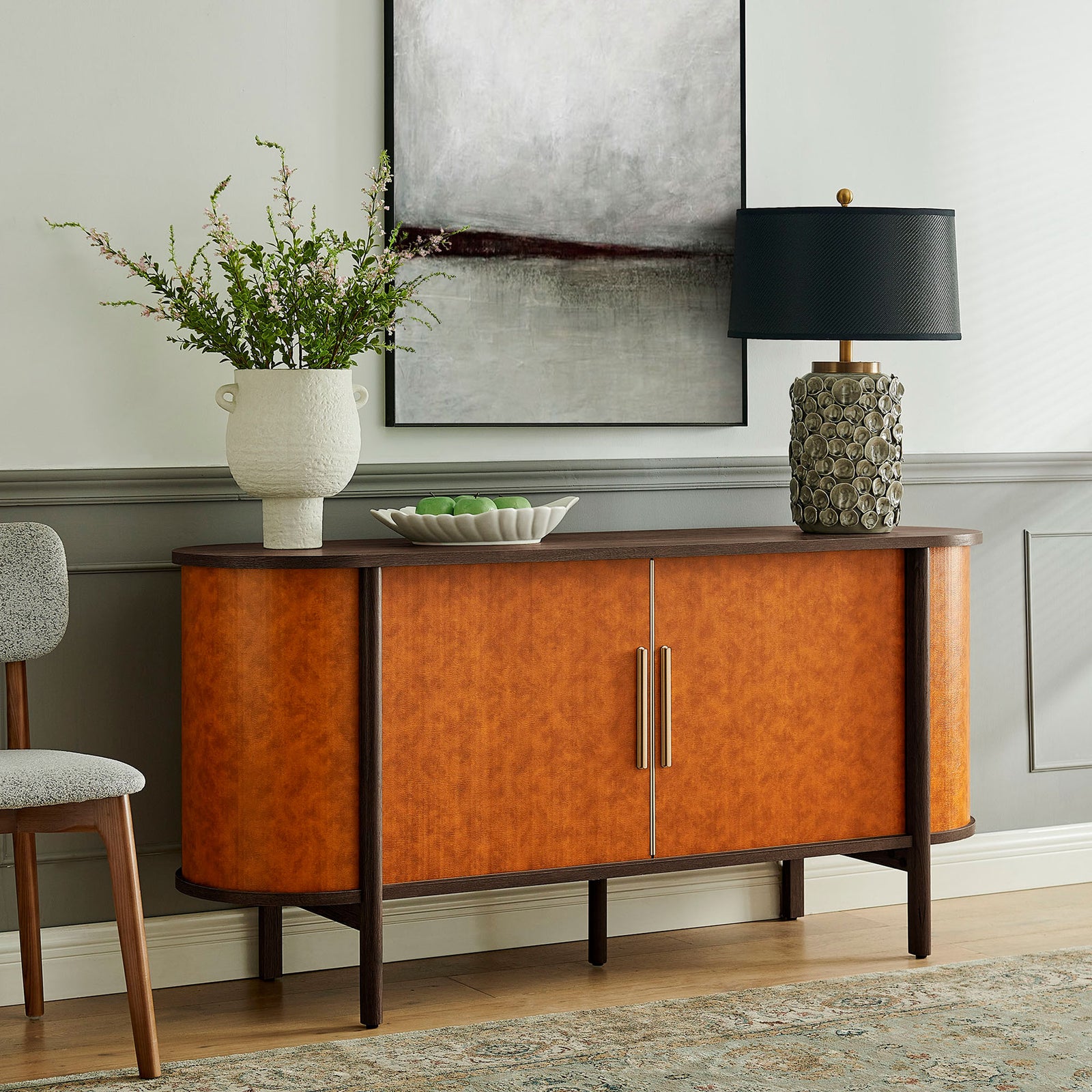Walnut tan oval sideboard styled in a modern living room with artwork, lamp, and vase for a finished look || EEI-7373-WAL-TAN || front_angle_room