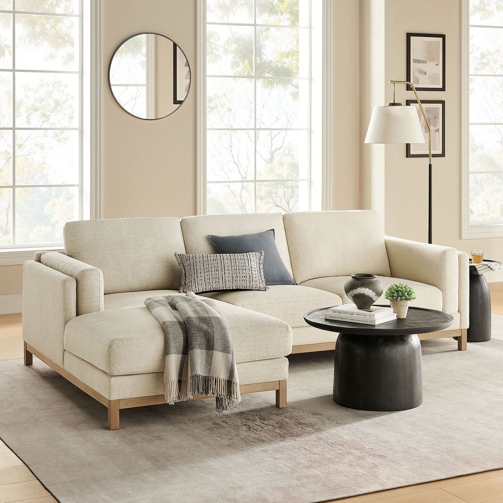 Ivory left-facing sectional in a bright living room, paired with a round black coffee table and neutral decor || EEI-7374-IVO || front_angle_room