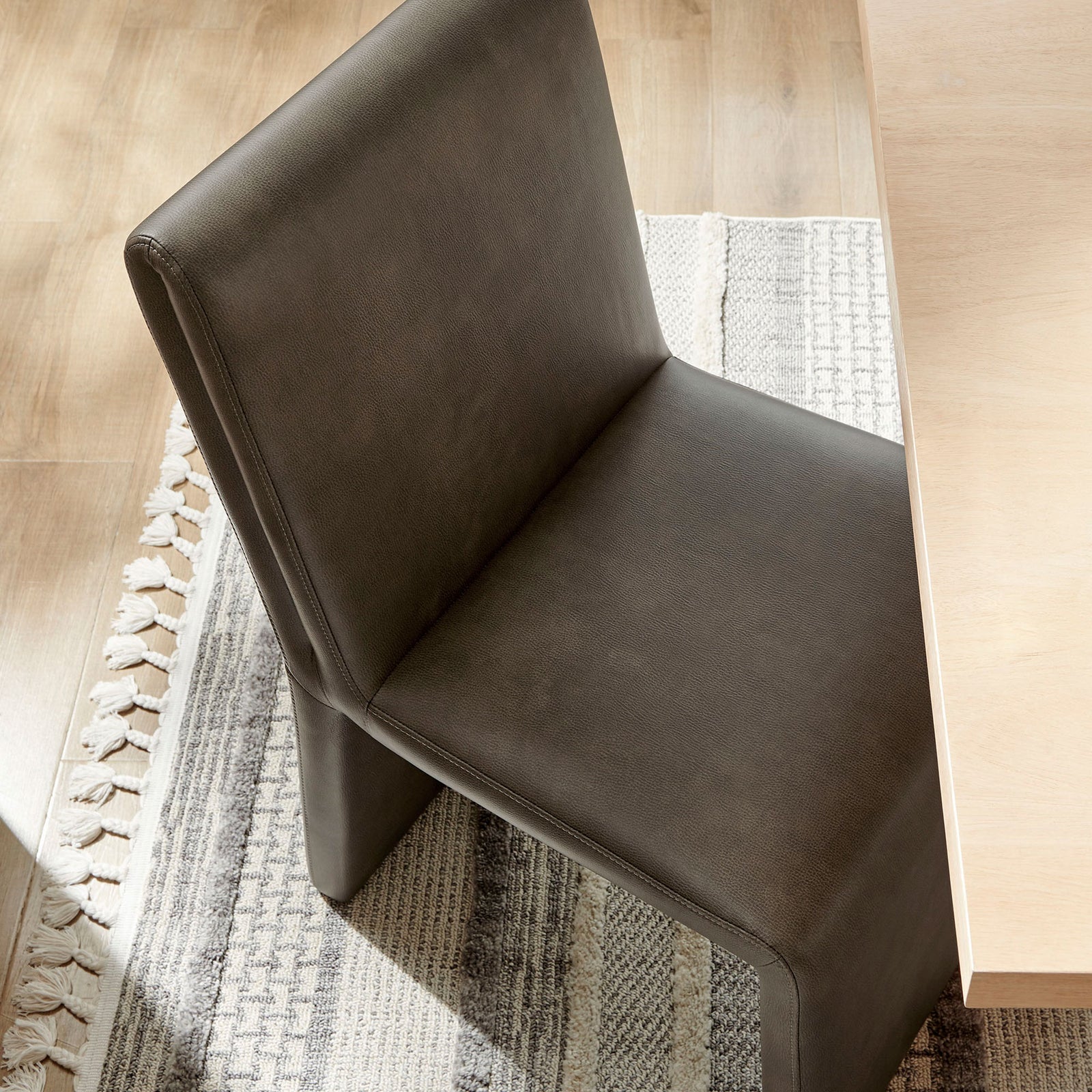 Emory dining chair pulled up to a light wood table, highlighting padded seat over a textured neutral rug || EEI-7385-MUS || top_angle_room