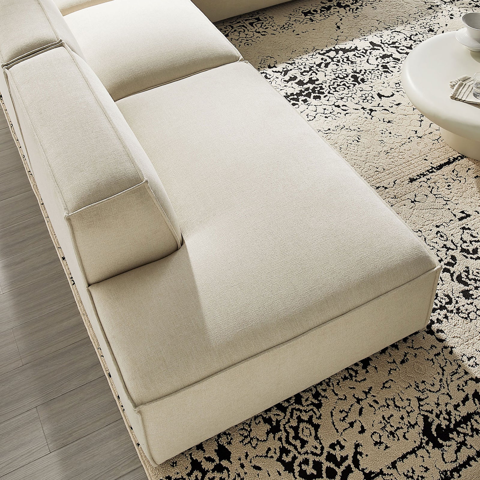 Generous chaise seat in ecru performance fabric layered over a patterned rug for relaxed lounging. || EEI-7413-ECR || detail_room