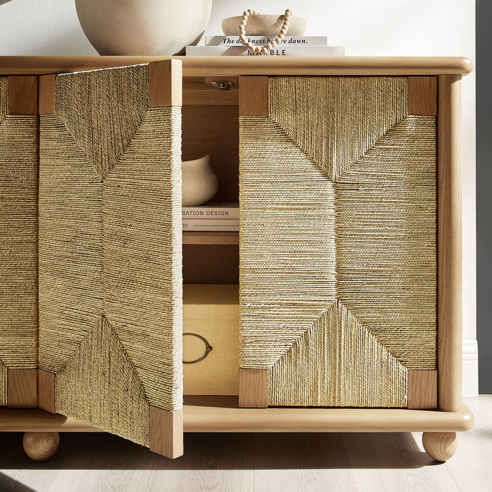 Seagrass doors partially open to reveal oak cabinet storage with styled books, boxes, and decor accents || EEI-7451-OAK || storage_open_room
