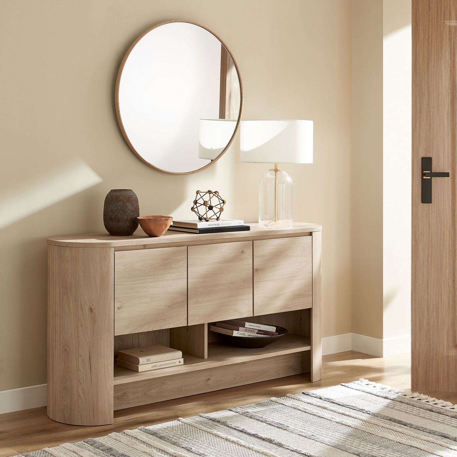 Light oak sideboard in an entryway vignette with round mirror, lamp, and decor accents || EEI-7478-LOA || front_room