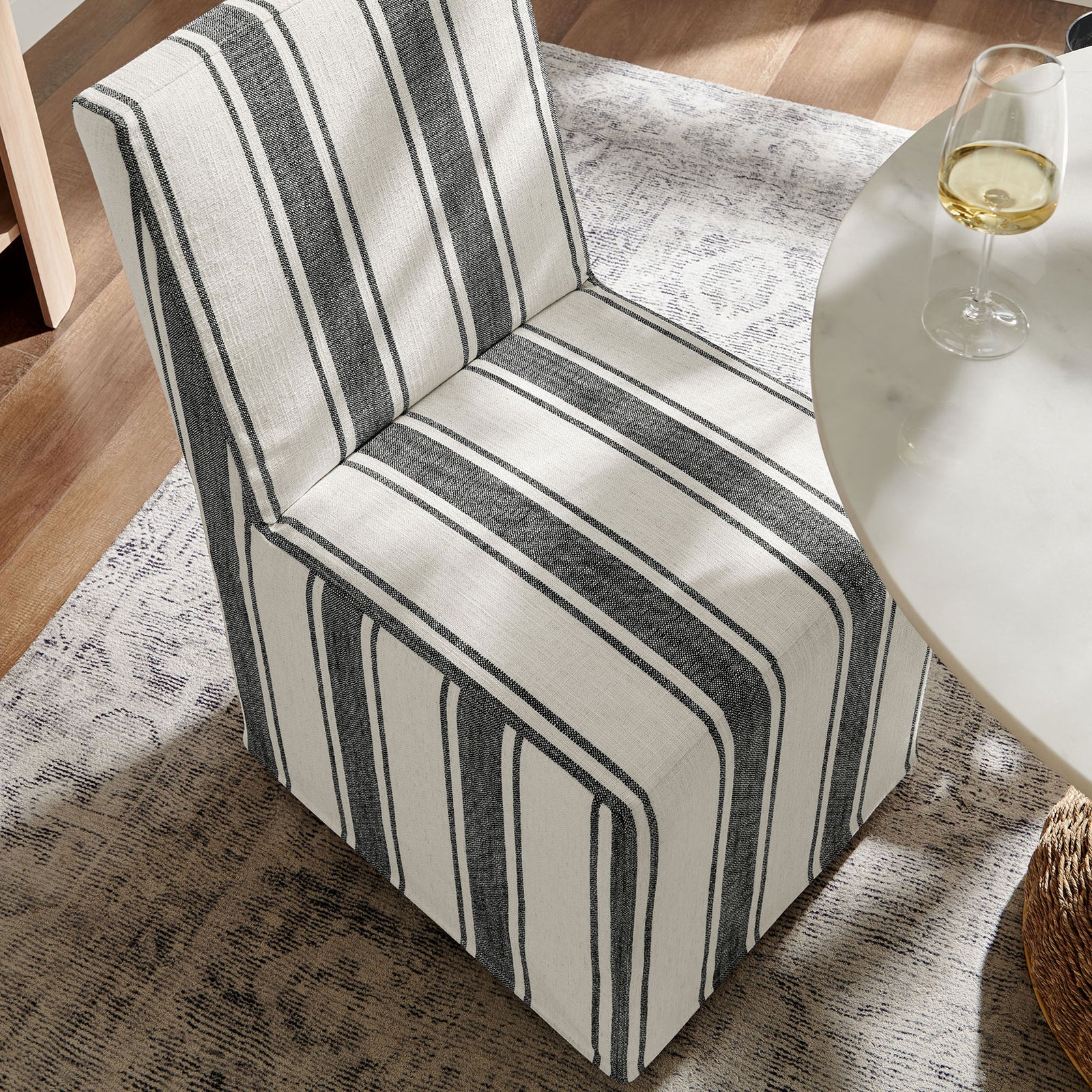 Striped slipcovered dining chair rolling easily into place beside a modern round dining table. || EEI-7486-BLK || front_angle_room