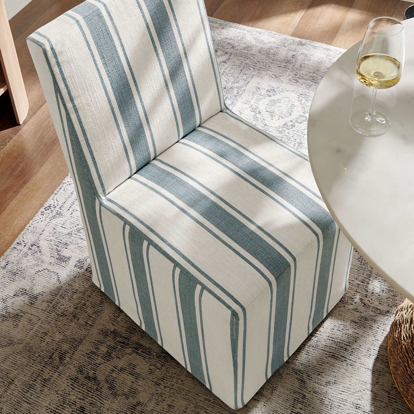 Striped slipcovered dining chair styled beside a modern round table in a bright, relaxed room || EEI-7486-BLU || front_angle_room
