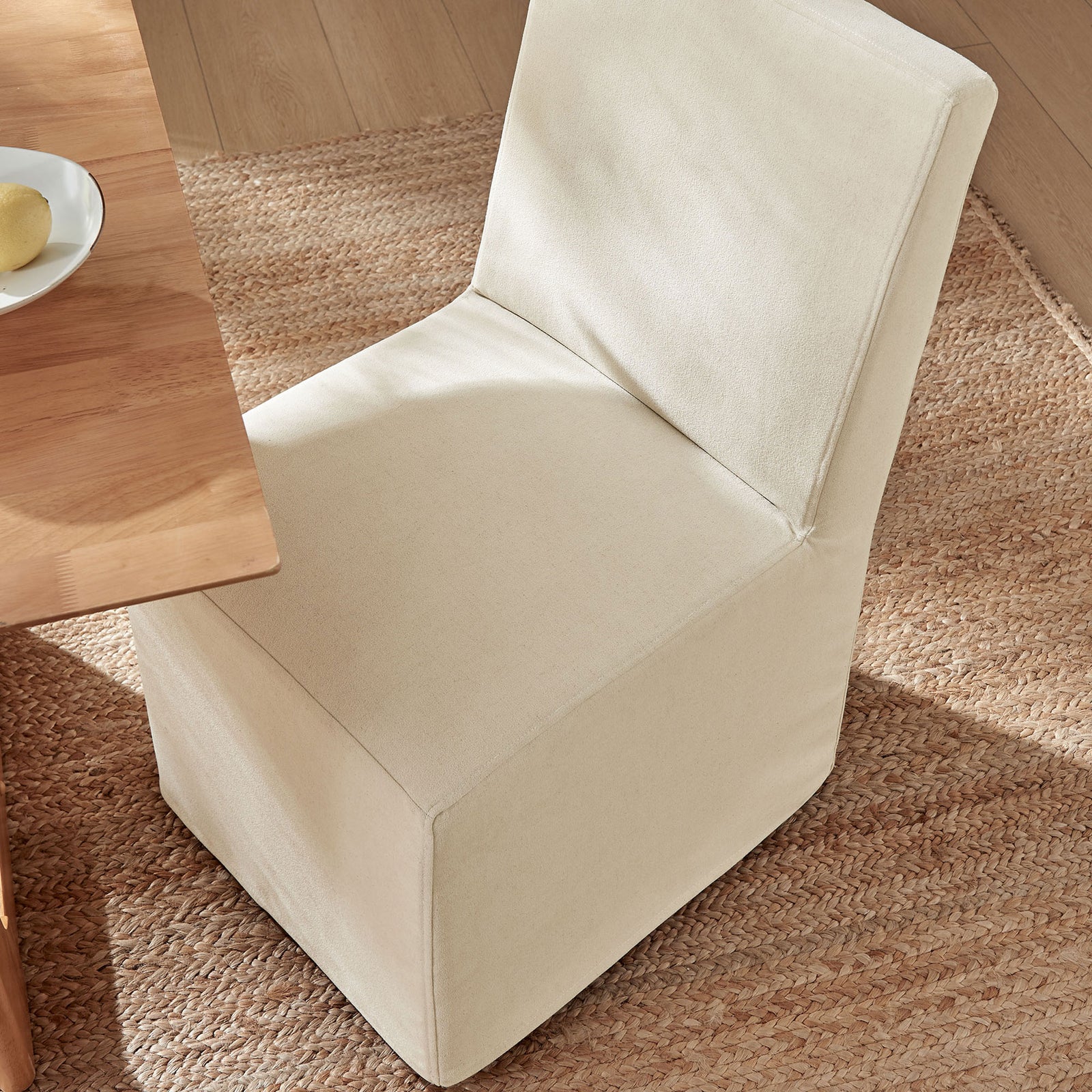 Slipcovered dining chair in a warm linen-blend fabric tucked neatly to a natural wood table on a woven rug. || EEI-7528-LIN || top_angle_room