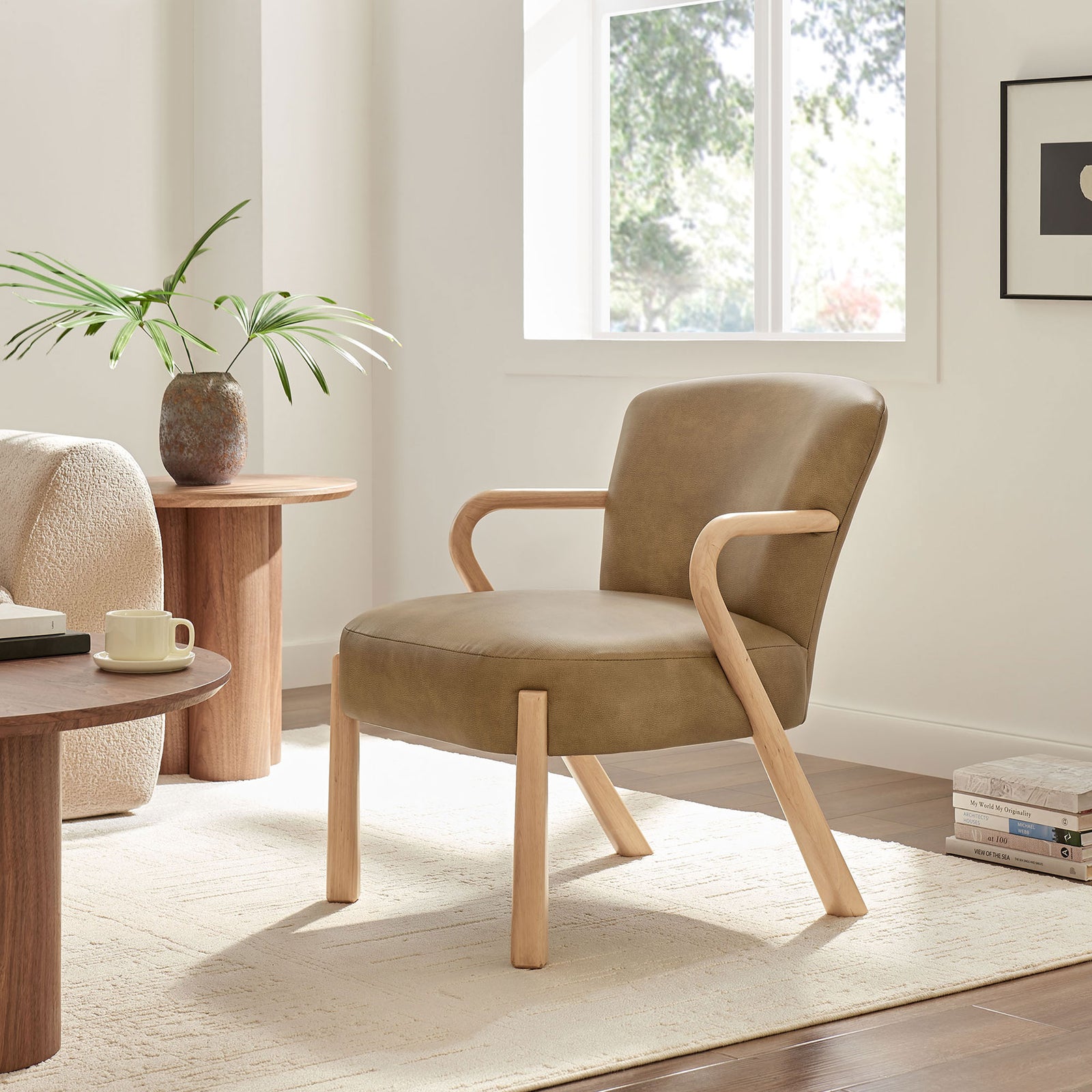 Accent chair styled in a bright living room, showcasing toast faux leather and curved wood arms || EEI-7529-TST || front_angle_room