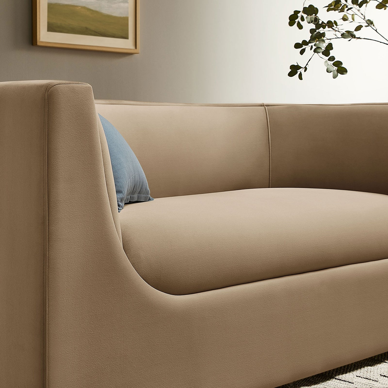 Detail of taupe velvet loveseat arm with blue accent pillow and greenery in a neutral room || EEI-7565-TAU || detail_room