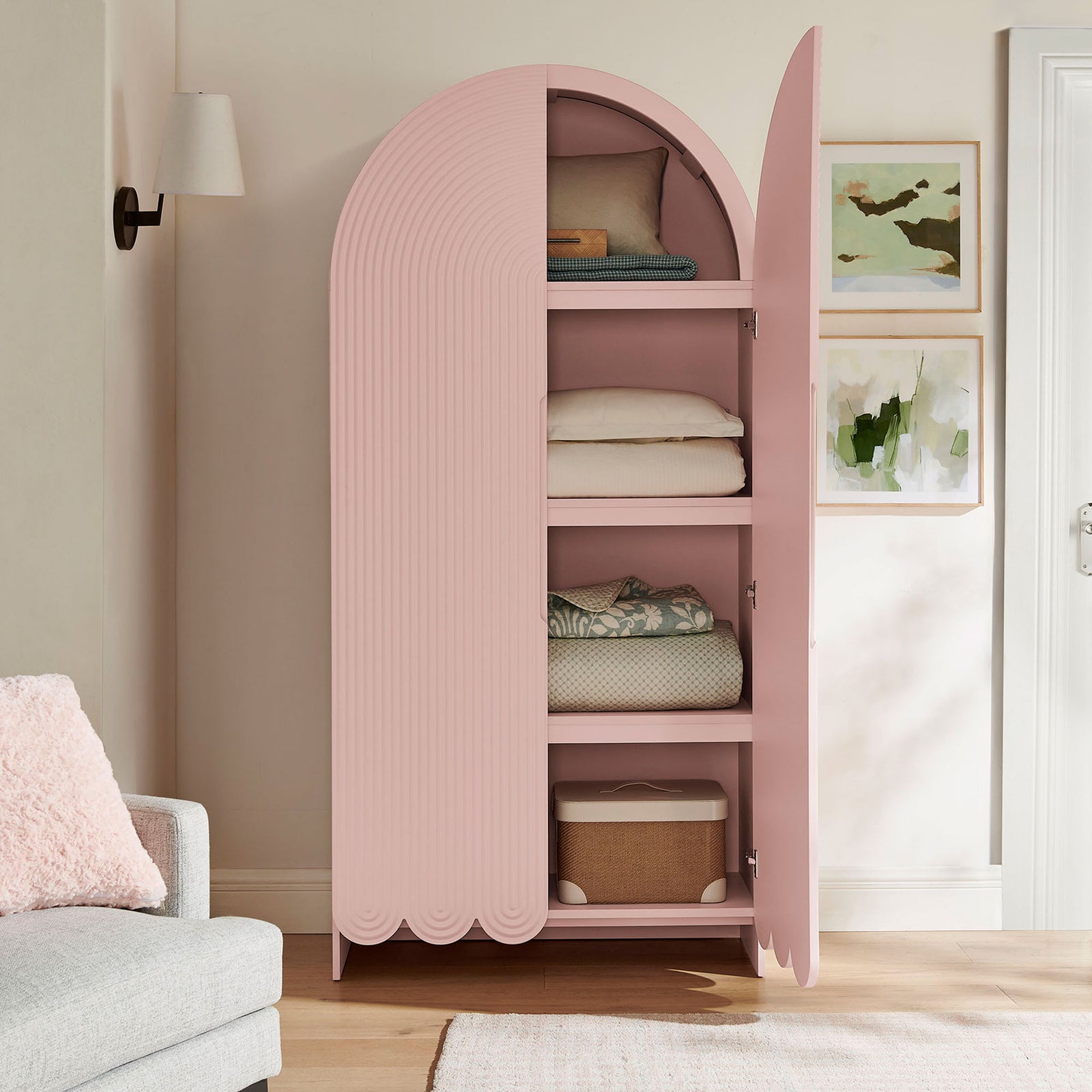 Soft pink arched cabinet with open doors neatly arranged with folded bedding and baskets || EEI-7570-SPN || front_open_room