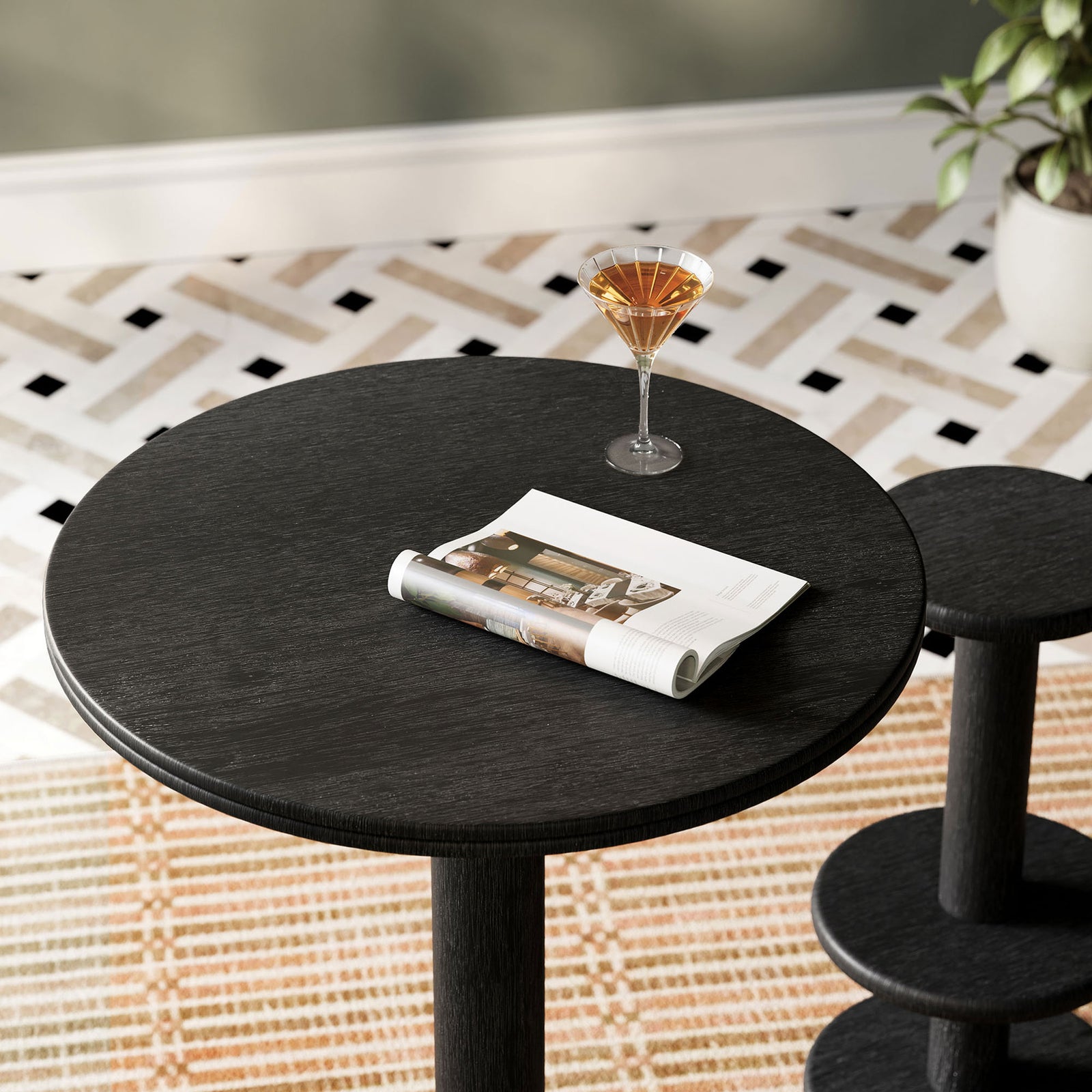 Black round bar table styled with cocktail and magazine, adding modern contrast over patterned rug. || EEI-7585-BLK || detail_room