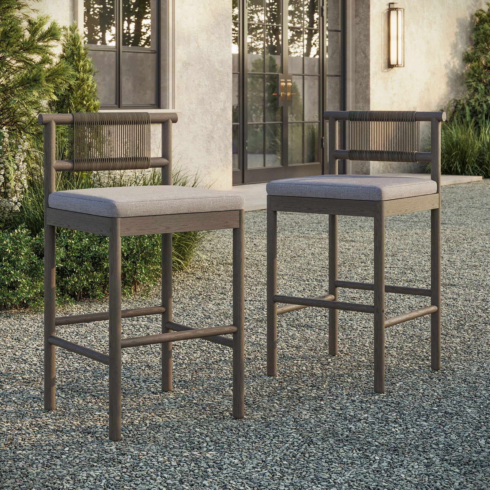 Pair of weathered gray bar stools grouped around an outdoor bar table on a gravel terrace || EEI-7626-WGR-PEB || front_angle_multi_room