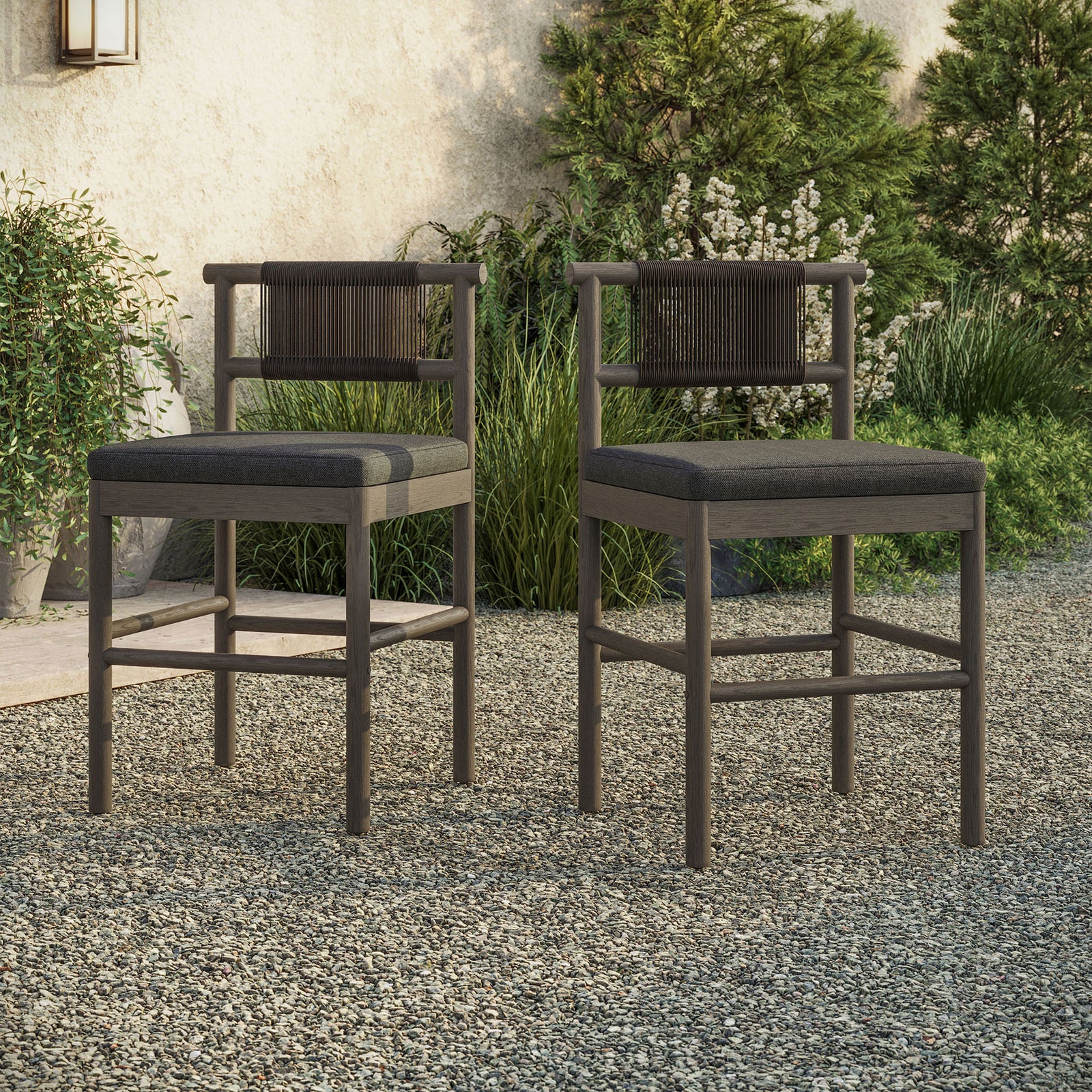 Pair of weathered gray counter stools at an outdoor bar table on gravel with greenery || EEI-7627-WGR-FLI || front_angle_multi_room