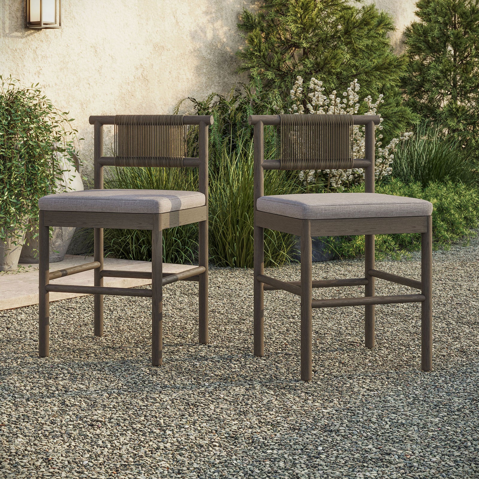 Pair of weathered gray counter stools arranged at an outdoor bar table on a gravel patio || EEI-7627-WGR-PEB || front_angle_multi_room