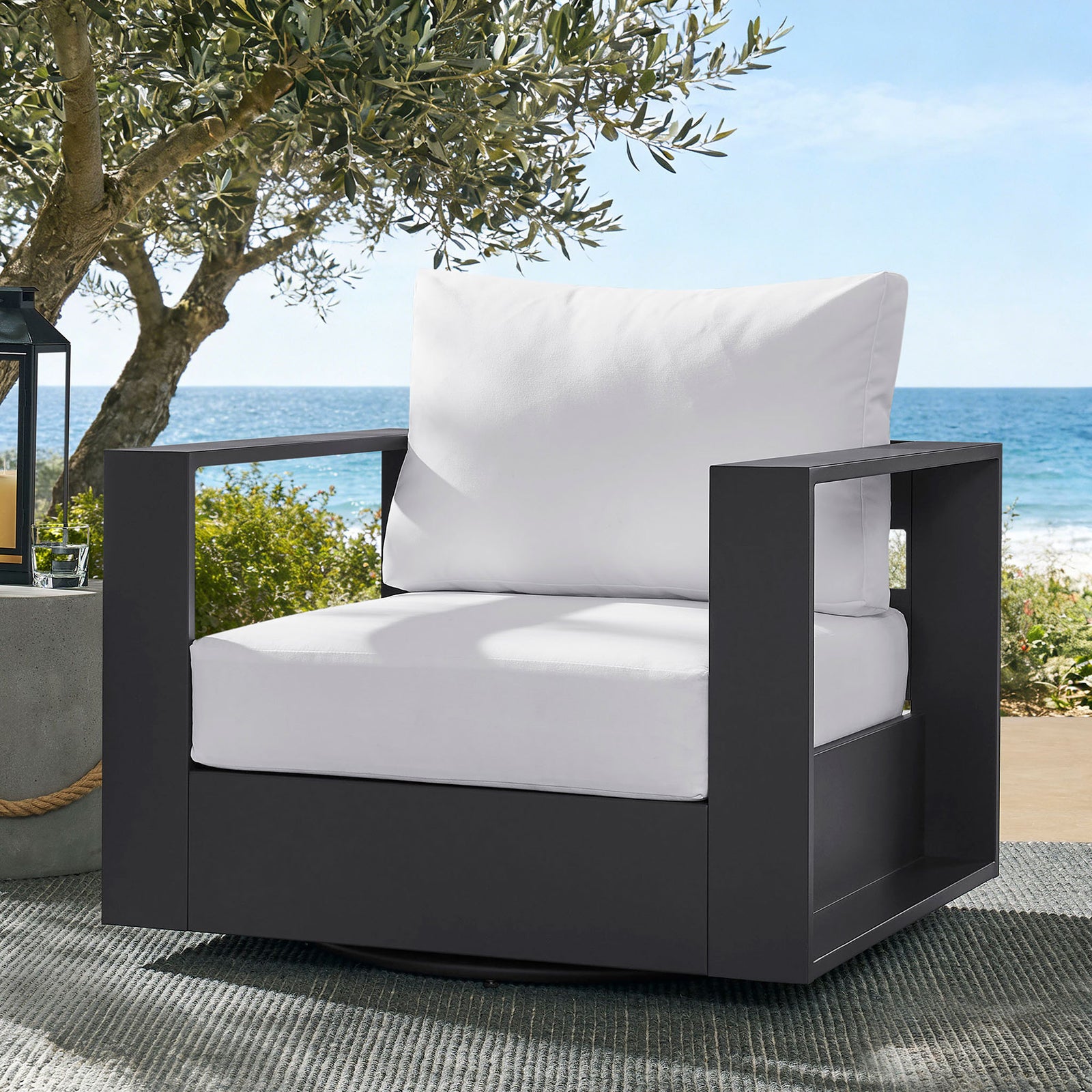 Tahoe swivel armchair with white cushions styled on breezy coastal patio with trees and ocean || EEI-7728-GRY-WHI || front_angle_room