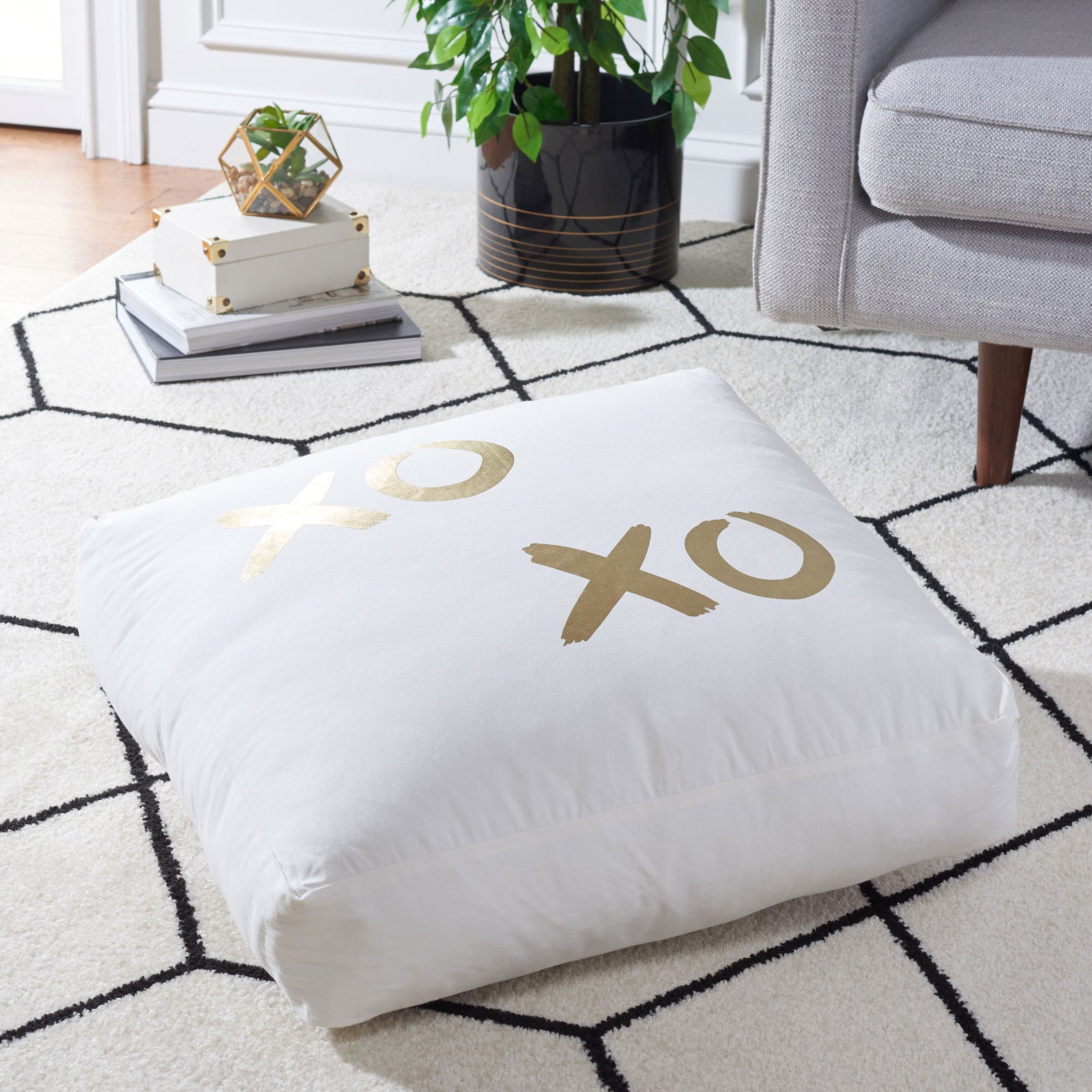 A plush floor pillow with gold X and O motifs offers inviting comfort atop a patterned rug. || FLP1016A || front_angle_room
