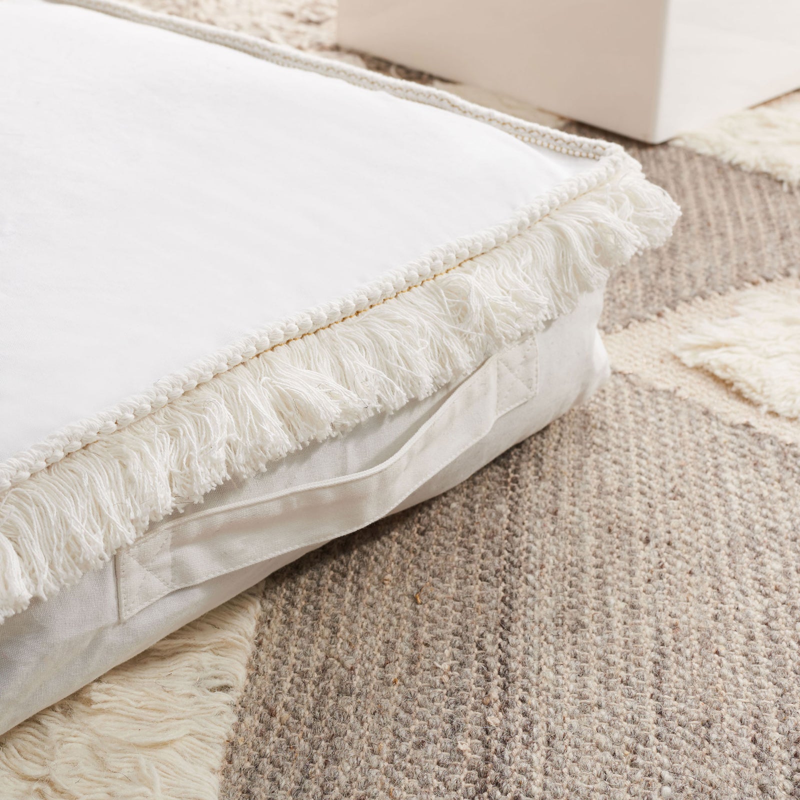 Fluffy ivory fringe and a slim fabric handle add texture and portability to this floor cushion. || FLP1018A || detail_room