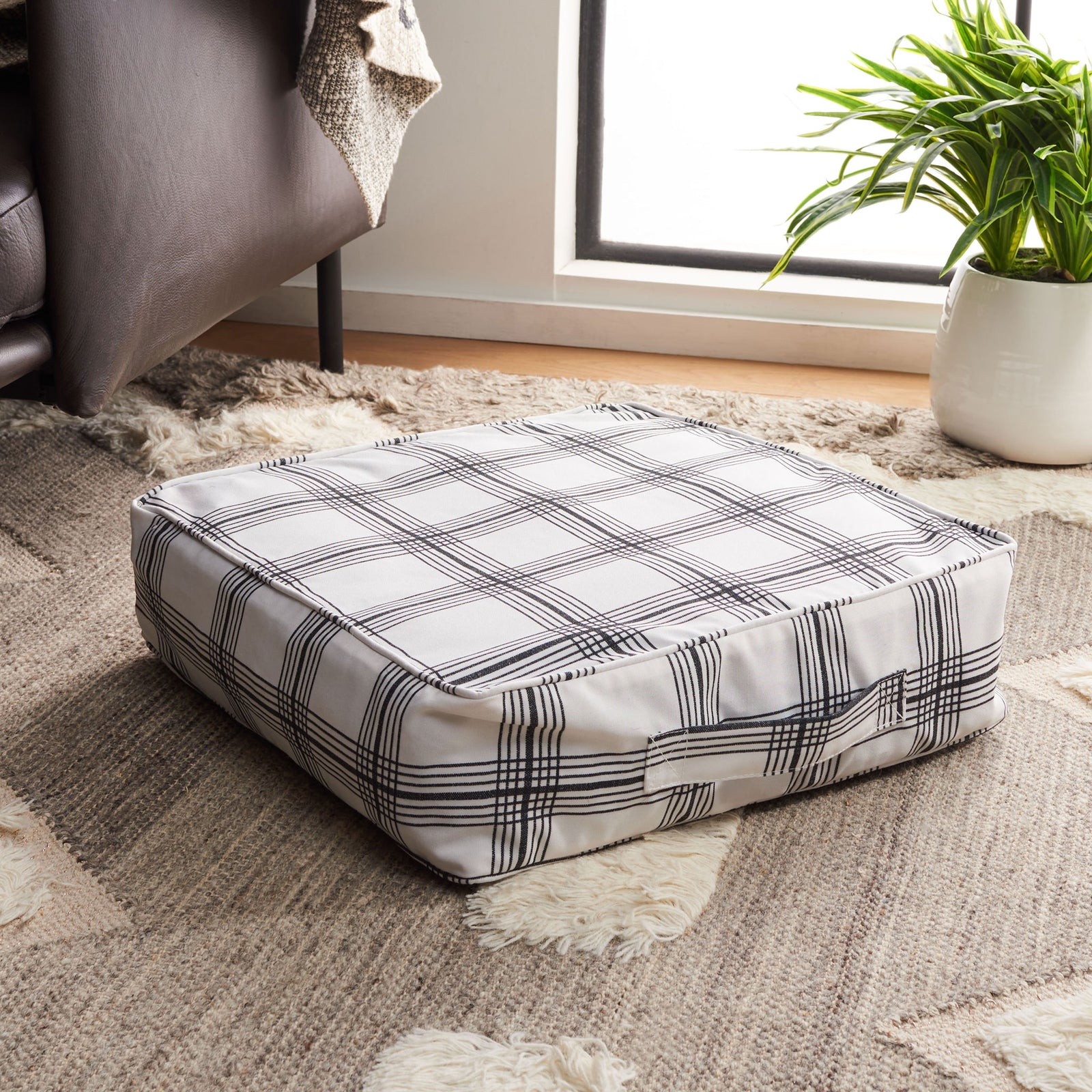 A generously cushioned square floor pillow pairs graphic plaid with a fabric carrying handle || FLP1020A || front_angle_room