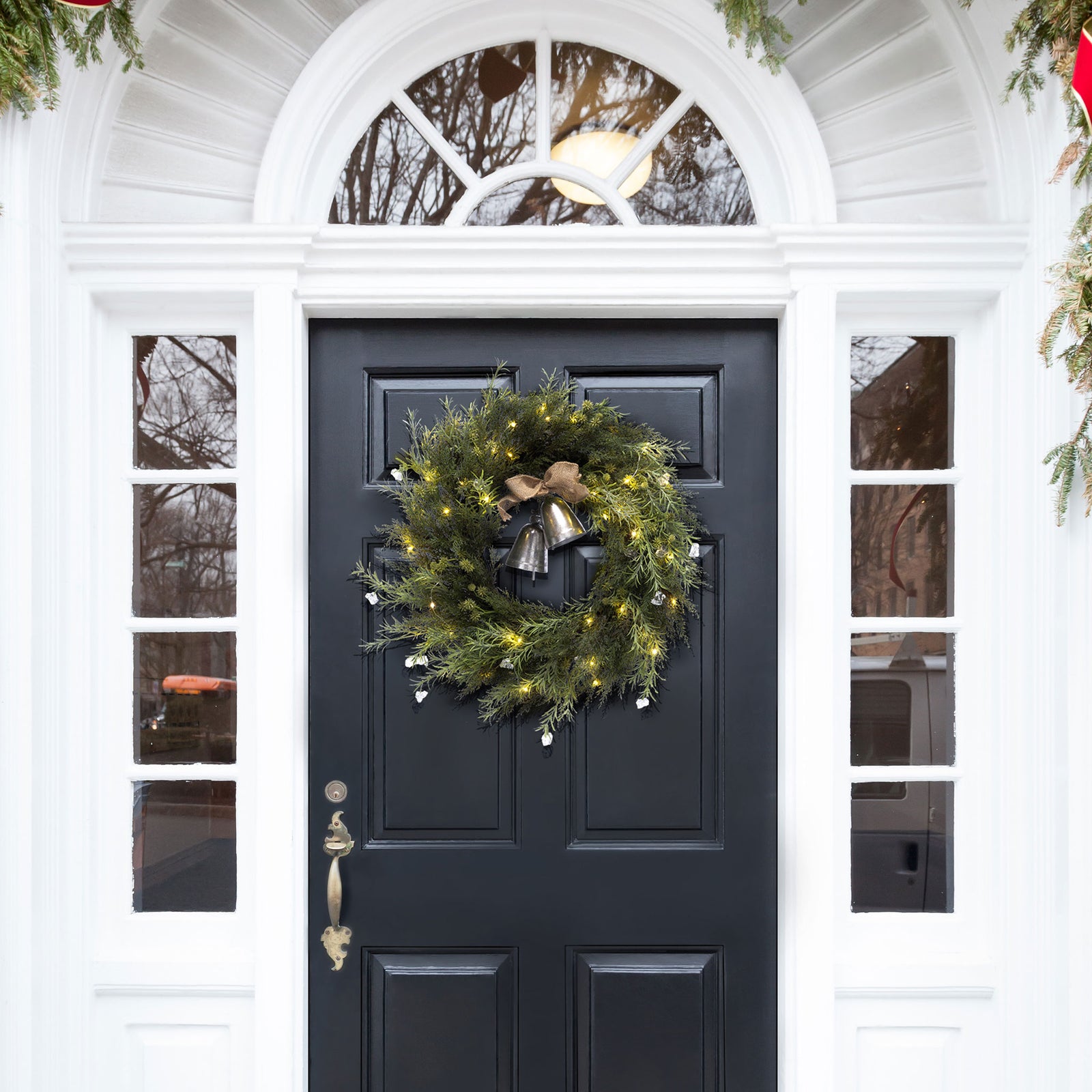 An illuminated evergreen wreath welcomes the season from a dark door. || FXP1096A || front_on_room