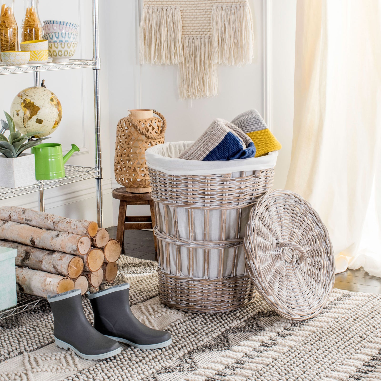 A whitewashed rattan hamper holds colorful textiles beside its removable woven lid. || HAC6500A || front_angle_open_room