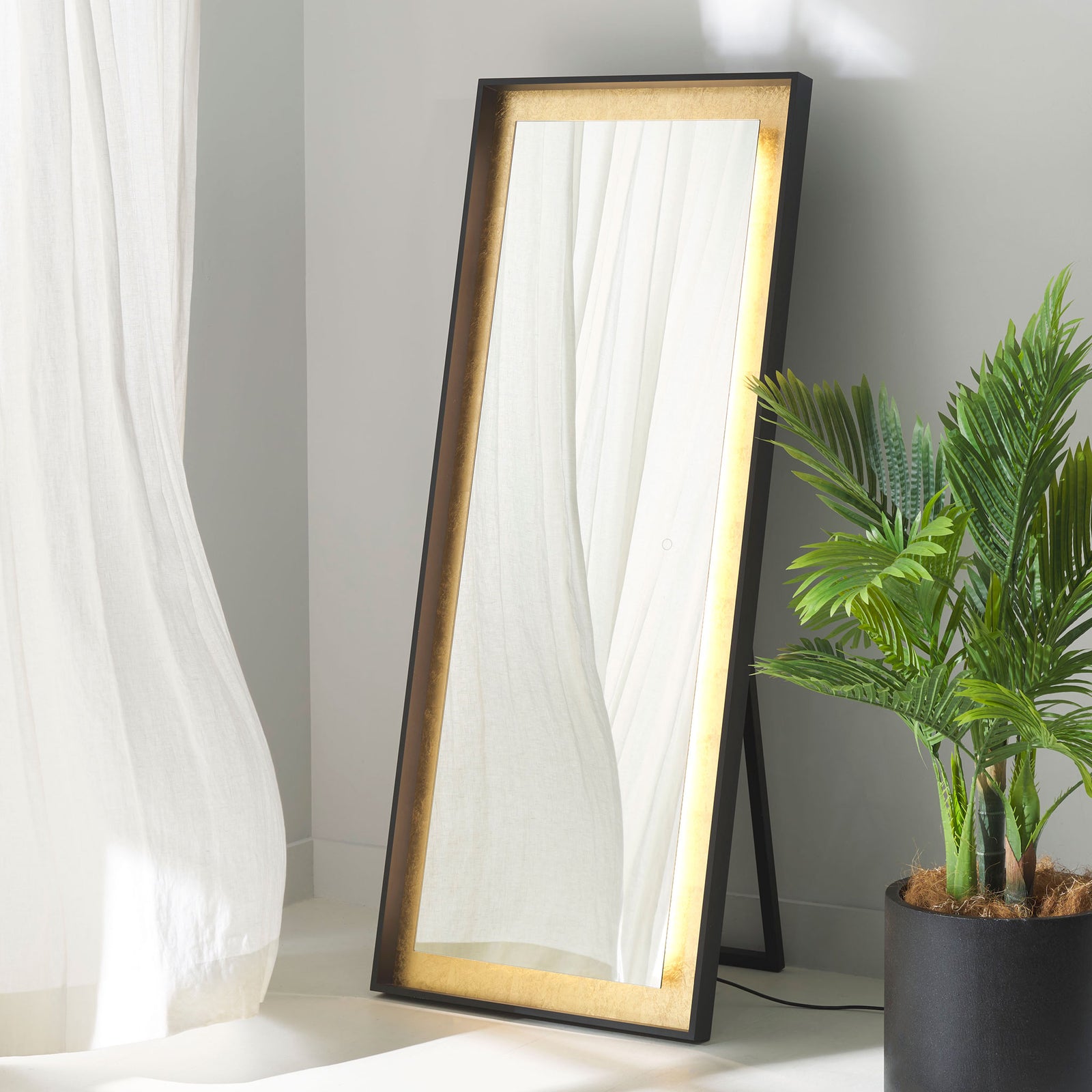 A glowing gold leaf border adds warm ambience to this black-framed freestanding mirror. || LMR1015B || front_angle_on_room