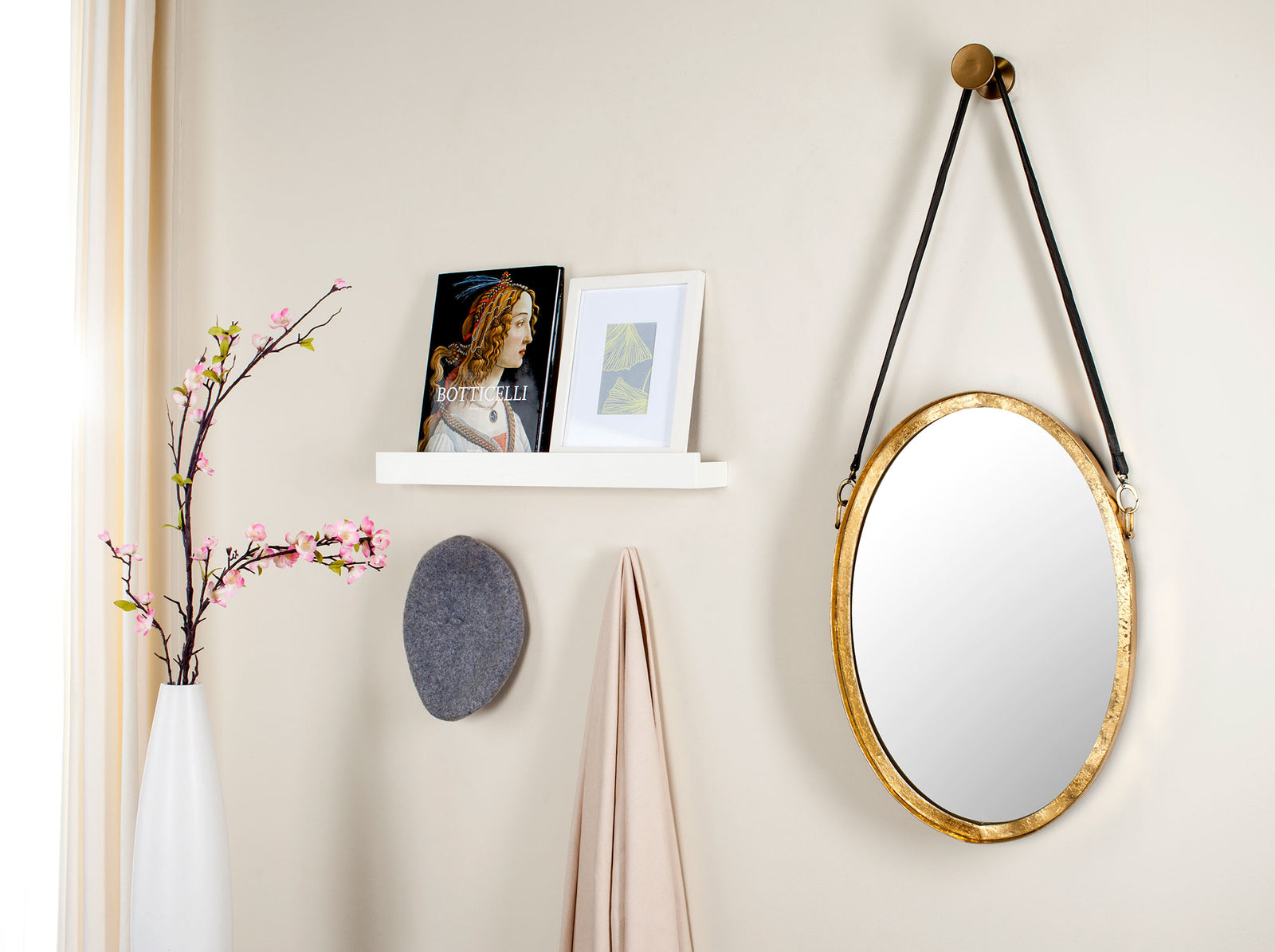 A gold-framed oval mirror with a black hanging strap brings warmth and depth to a bright wall. || MIR4066A || front_room
