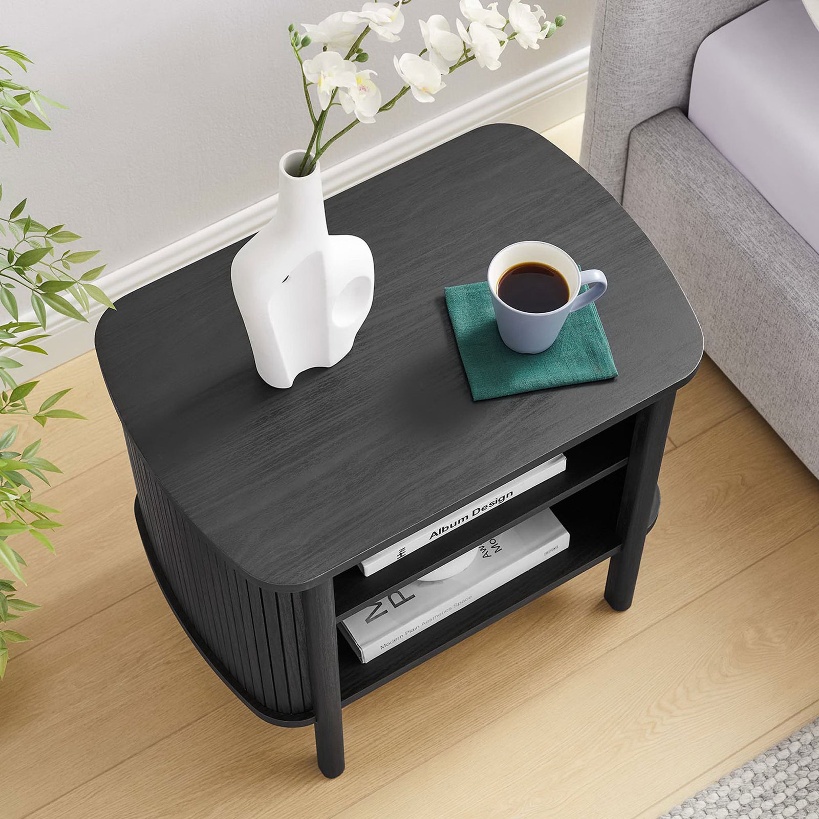 Black fluted nightstand in a bright room, surface styled with decor and a drink on a coaster || MOD-7157-BLK || top_angle_room