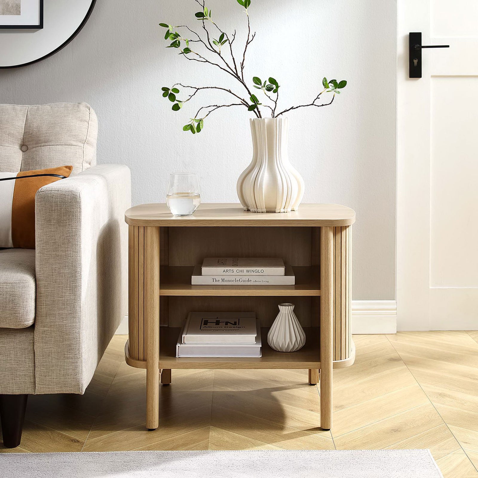 Cadence oak nightstand used as a living room side table, displaying decor and books on its open, airy shelving || MOD-7157-OAK || front_angle_room