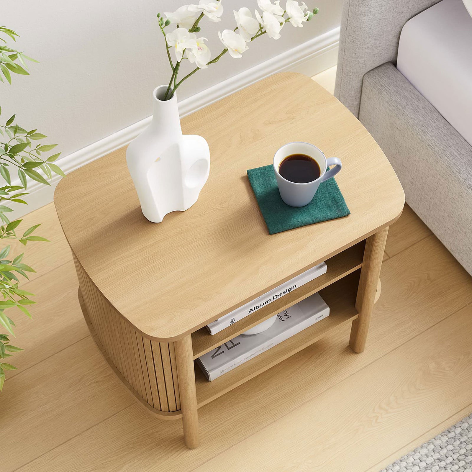 Styled Cadence oak nightstand with books, vase, and coffee, showcasing generous tabletop and open storage in use || MOD-7157-OAK || top_angle_room