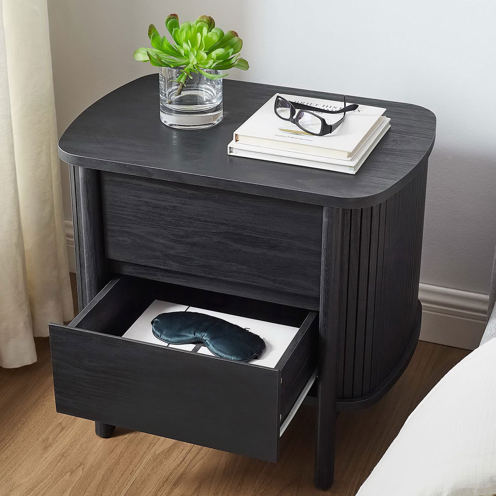 Black Cadence nightstand beside a bed with lower drawer open, keeping nighttime essentials neatly tucked away || MOD-7158-BLK || front_angle_open_room