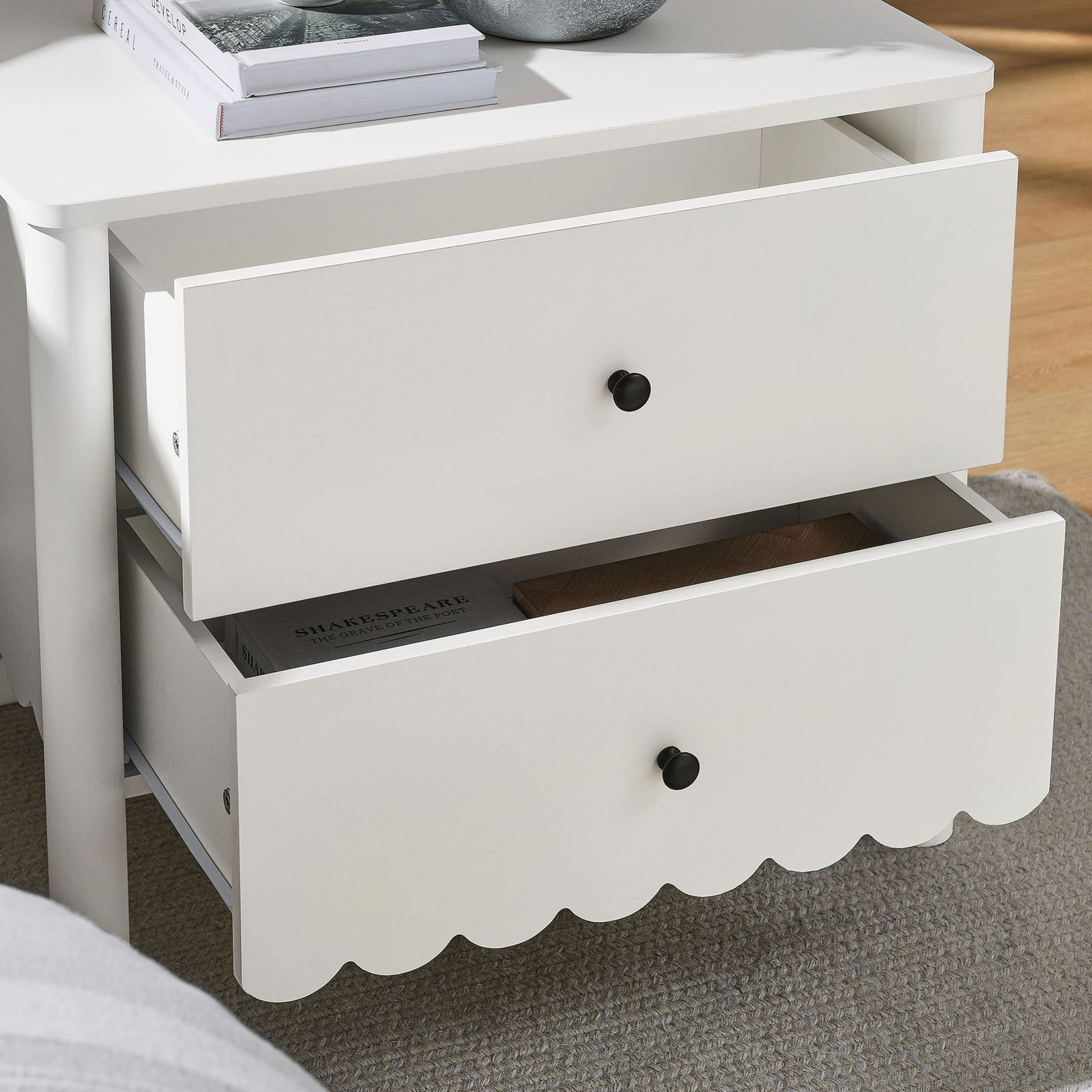 White scalloped nightstand with drawers open beside a bed on a soft neutral rug || MOD-7206-WHI || front_angle_open_room