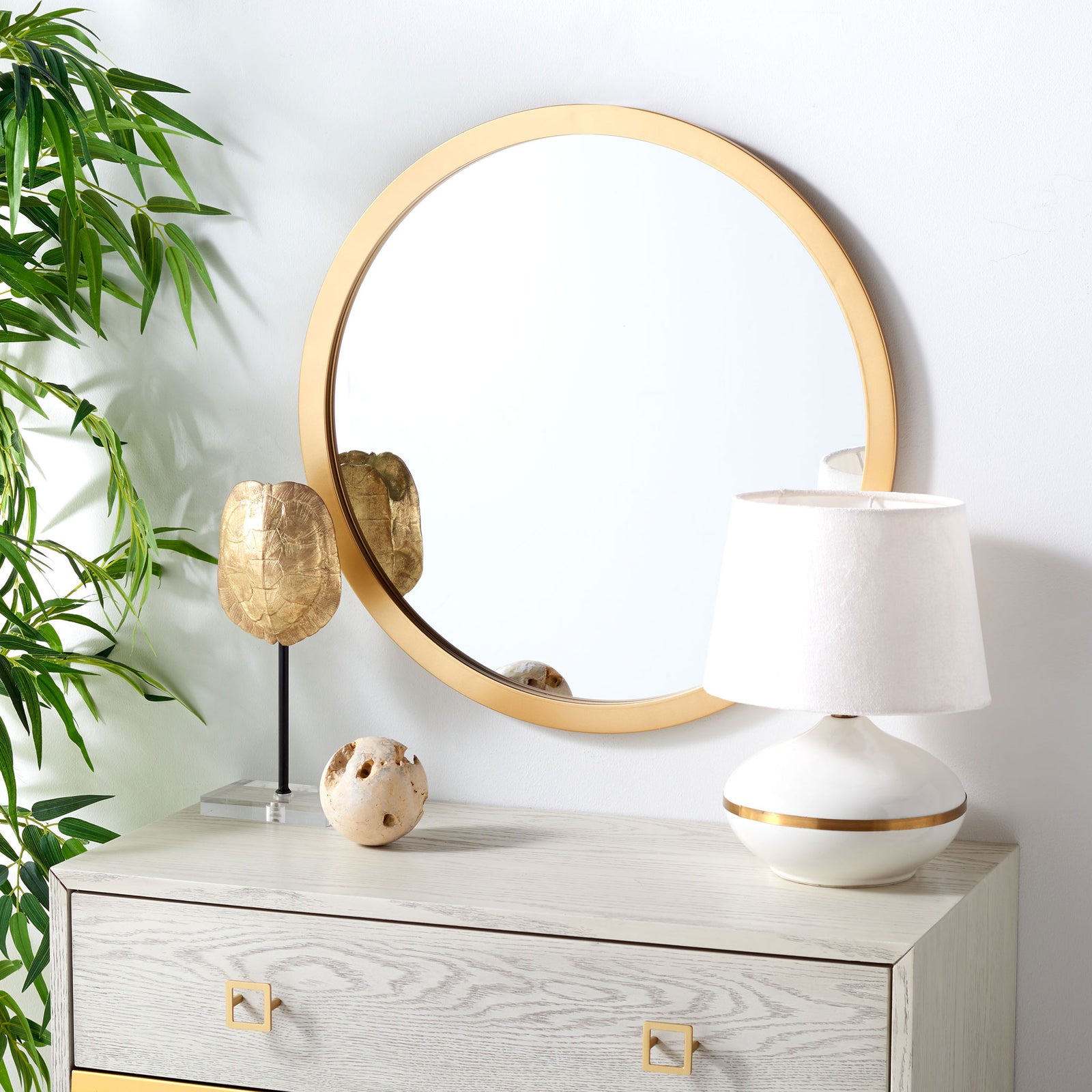 A round brass-finish mirror brightens the wall above a light-toned wood cabinet || MRR2006B || front_angle_room