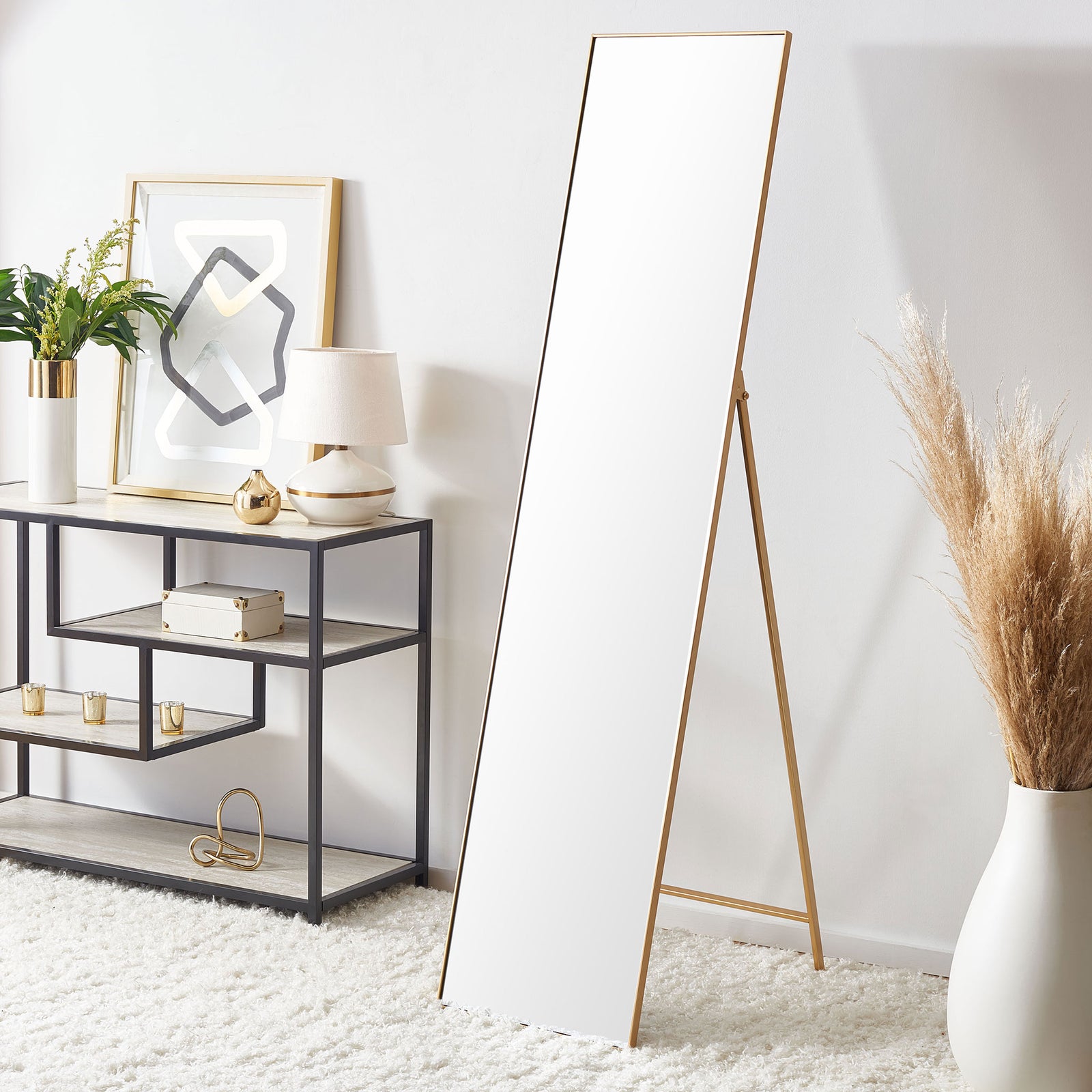 A tall brass-framed mirror with a freestanding support brings warm metallic style to a bright room || MRR2008A || front_angle_room