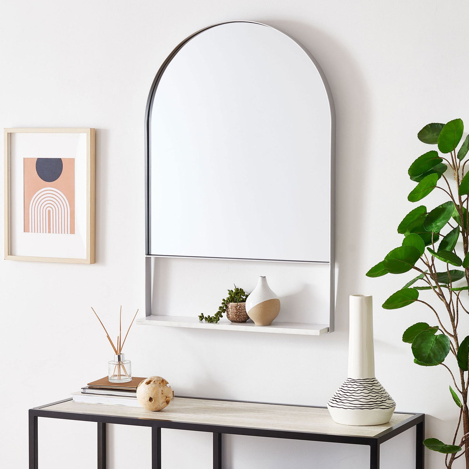 A silver-framed arched mirror hangs above a console, with a white shelf for small decor. || MRR2009D || front_room