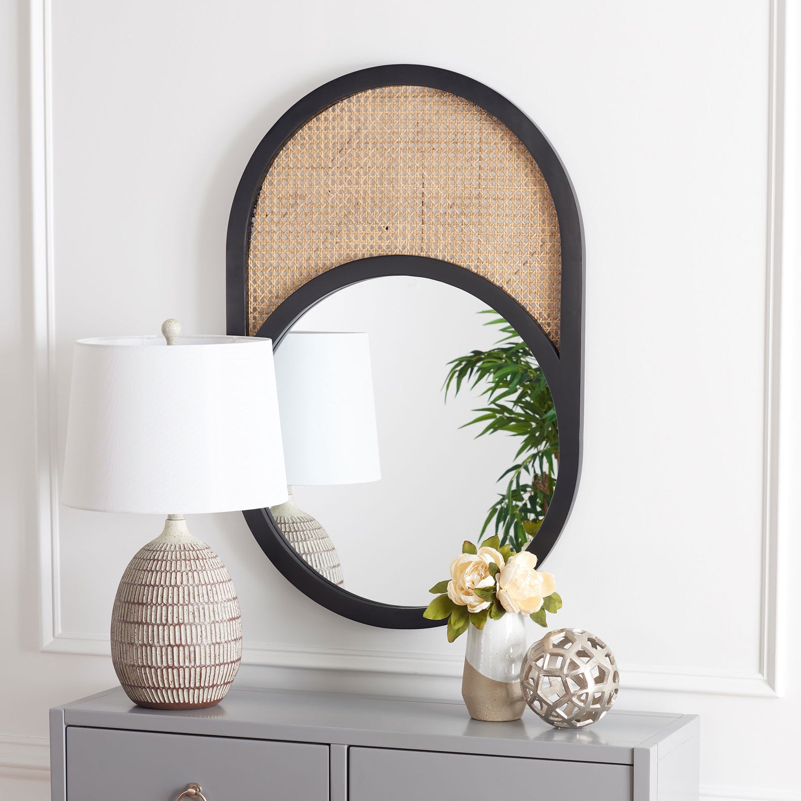 A black oval mirror with woven cane above the glass adds contrast and texture to a console wall. || MRR2019A || front_room