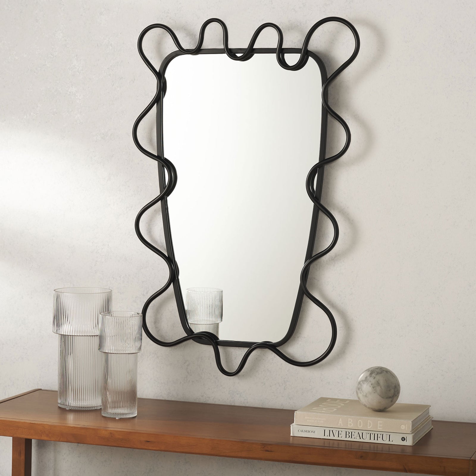 A tall mirror with flowing black metal trim brings sculptural style above a wood console || MRR2500A || front_room