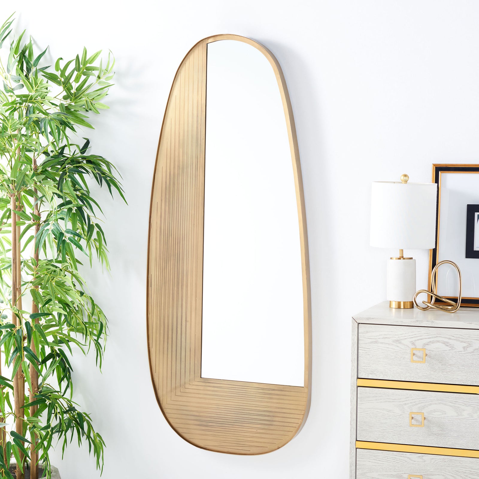 Curved brass-finish wall mirror adds sculptural warmth beside a light-toned dresser || MRR3067A || front_room