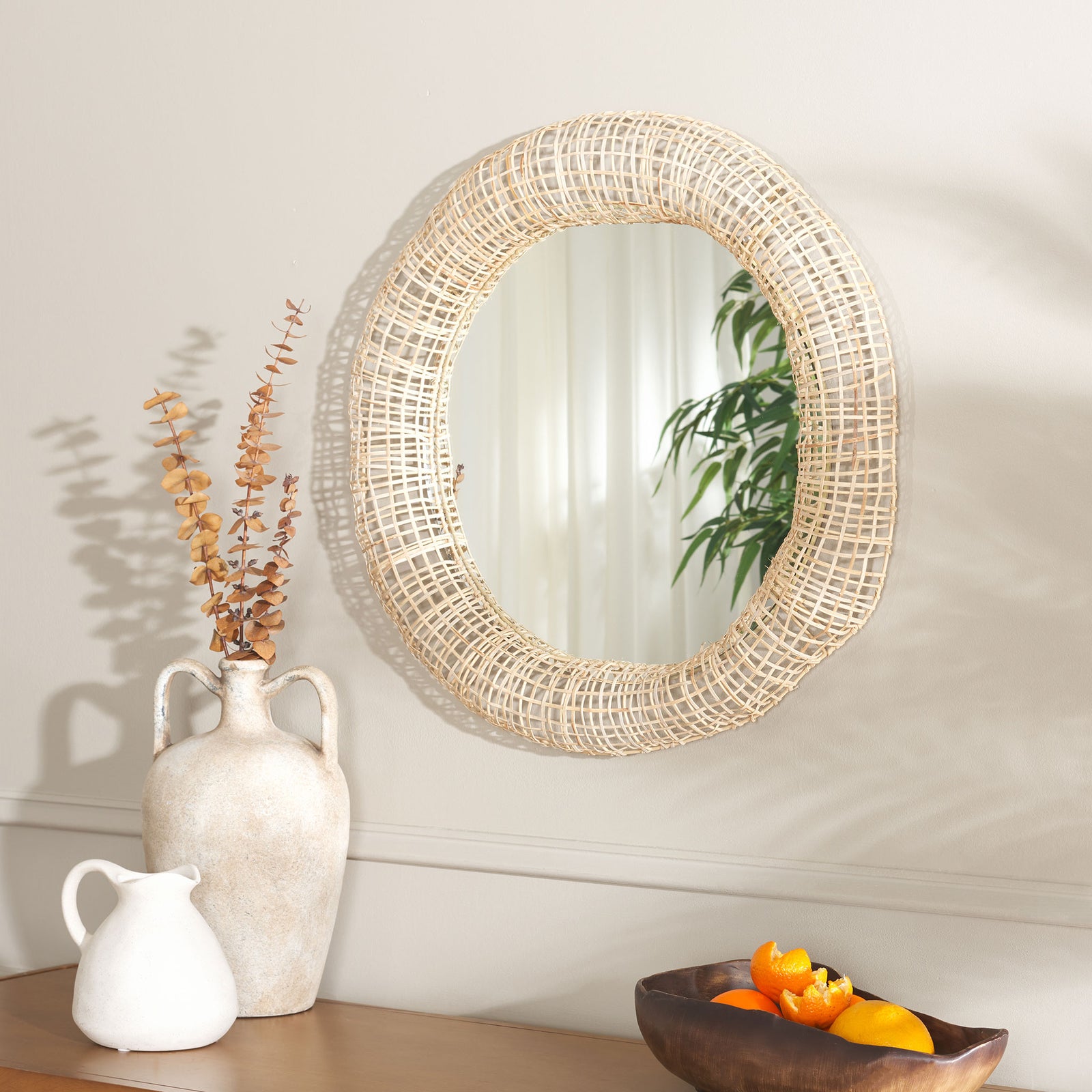 Natural cane lattice frames a round wall mirror above a tabletop with decorative vases || MRR4001A || front_angle_room