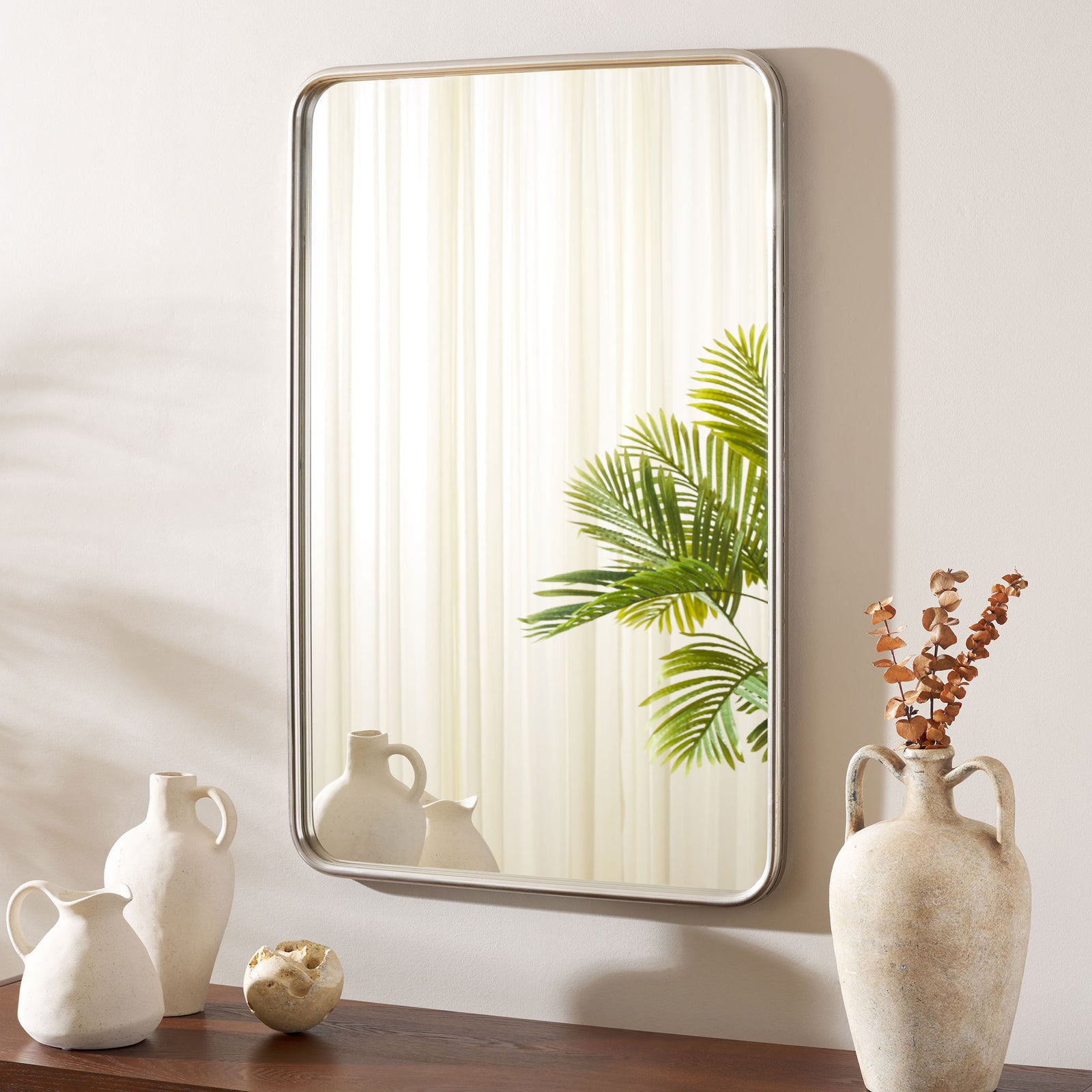 Chrome-framed wall mirror reflects greenery above a display of sculptural vases || MRR4006A || front_room