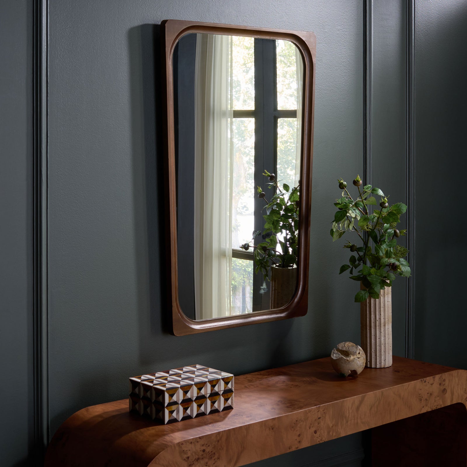 Warm brown wall mirror reflects natural light above a sculptural wood console || MRR9031A || front_angle_room