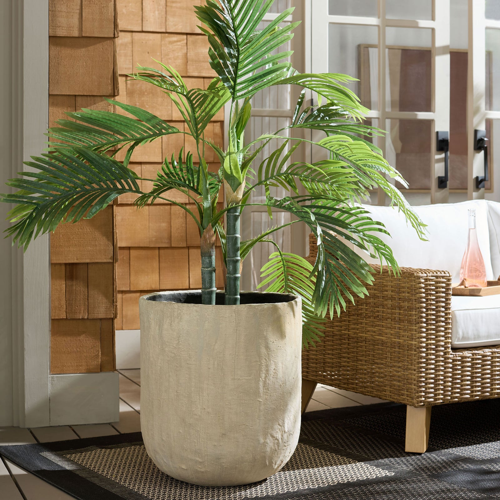 Tropical greenery fills a generous beige planter beside a woven lounge chair. || PAT1405B || front_room