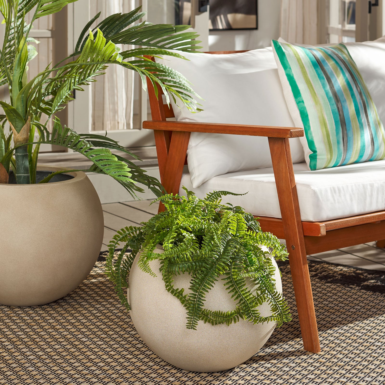 Fern-filled beige orb planter adds greenery beside a larger matching planter and wood-framed seating. || PAT1518B || front_series_room