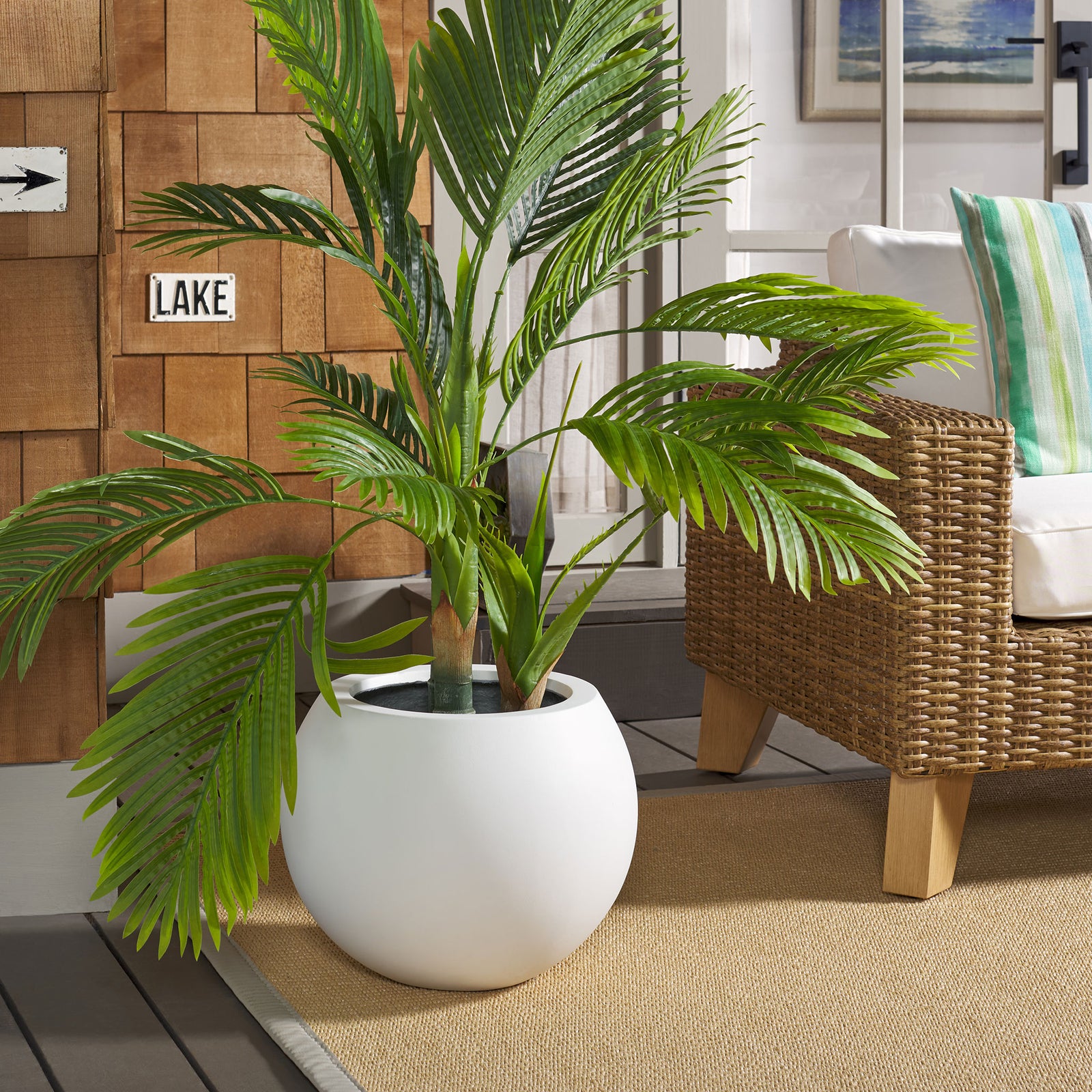 A crisp white orb planter showcases tall palm leaves alongside woven patio seating. || PAT1518C || front_room