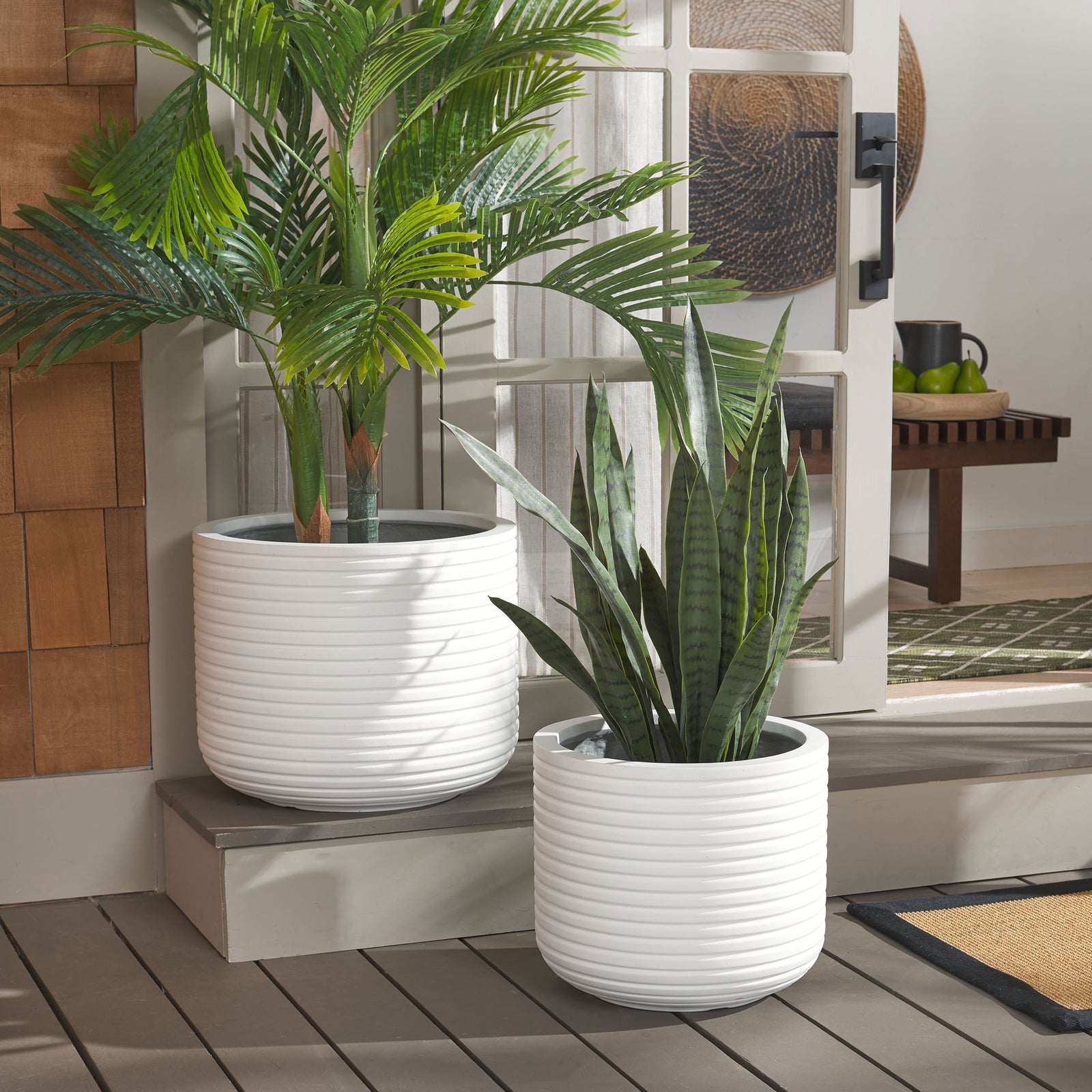 A pair of white ribbed planters displays leafy palms and upright foliage by a sunny doorway || PAT1530C-SET2 || front_angle_room